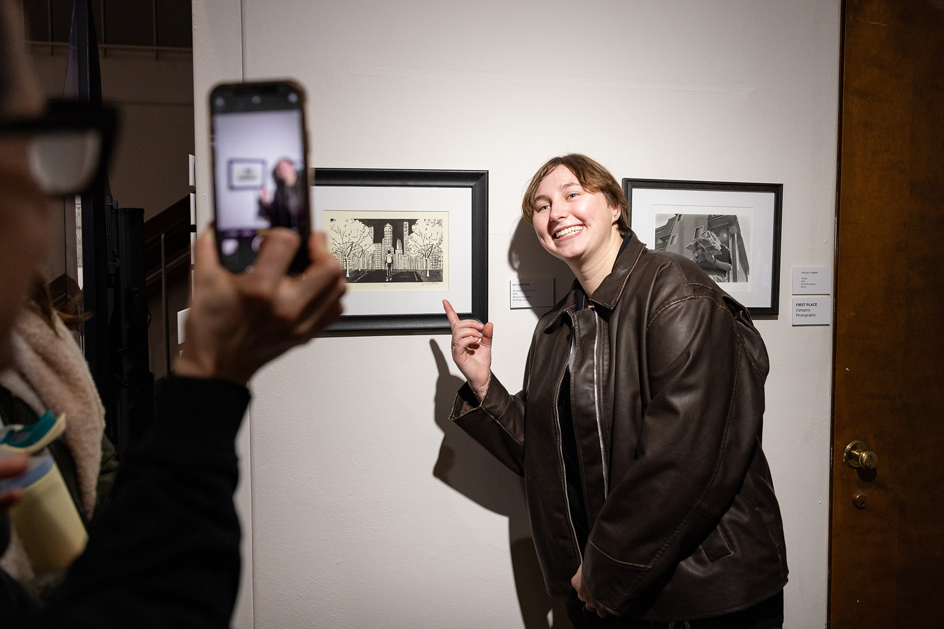 Someone takes a photo of a person smiling and pointing at a piece of art