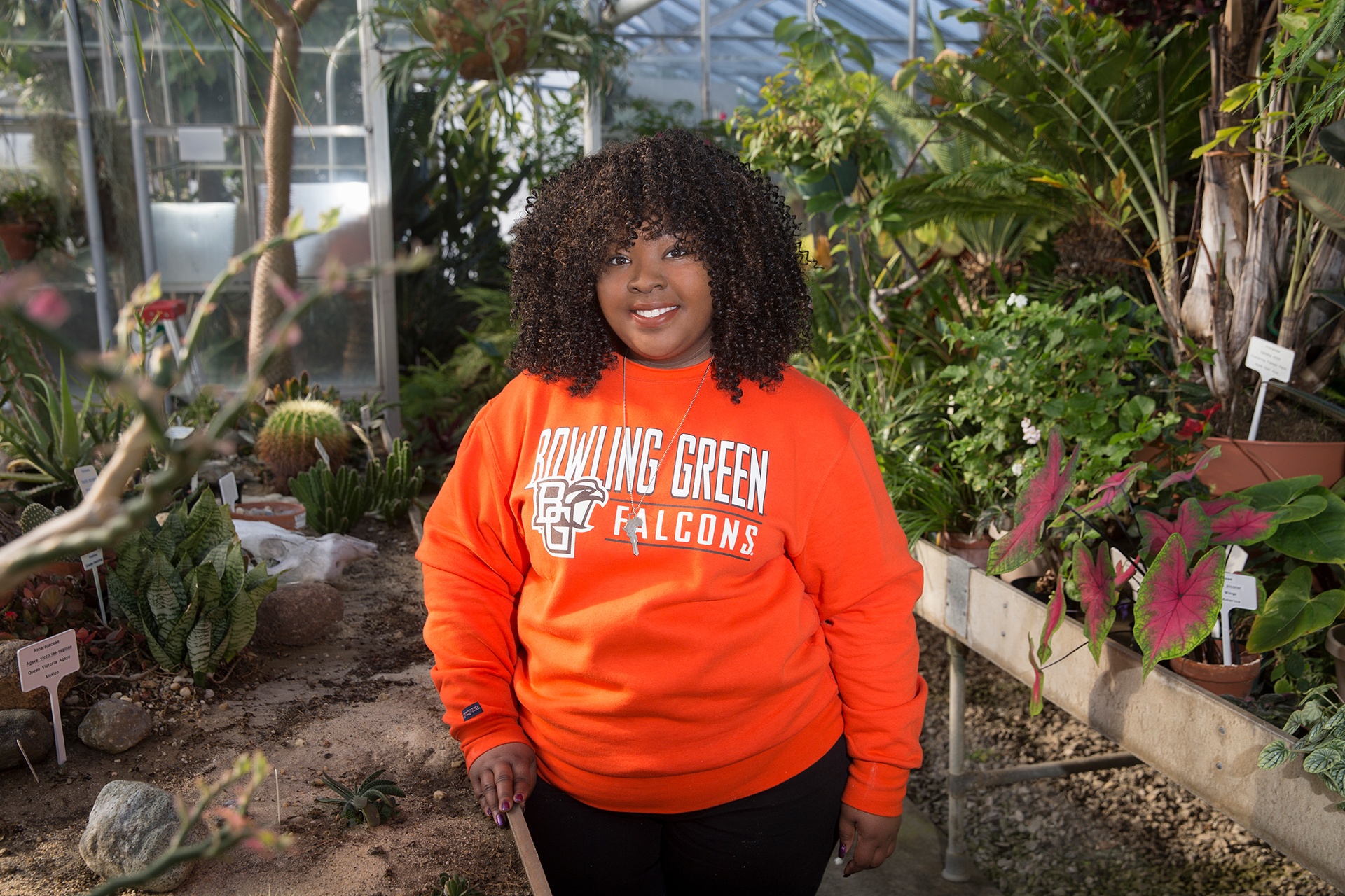Student standing in front of plants in a greenhouse.