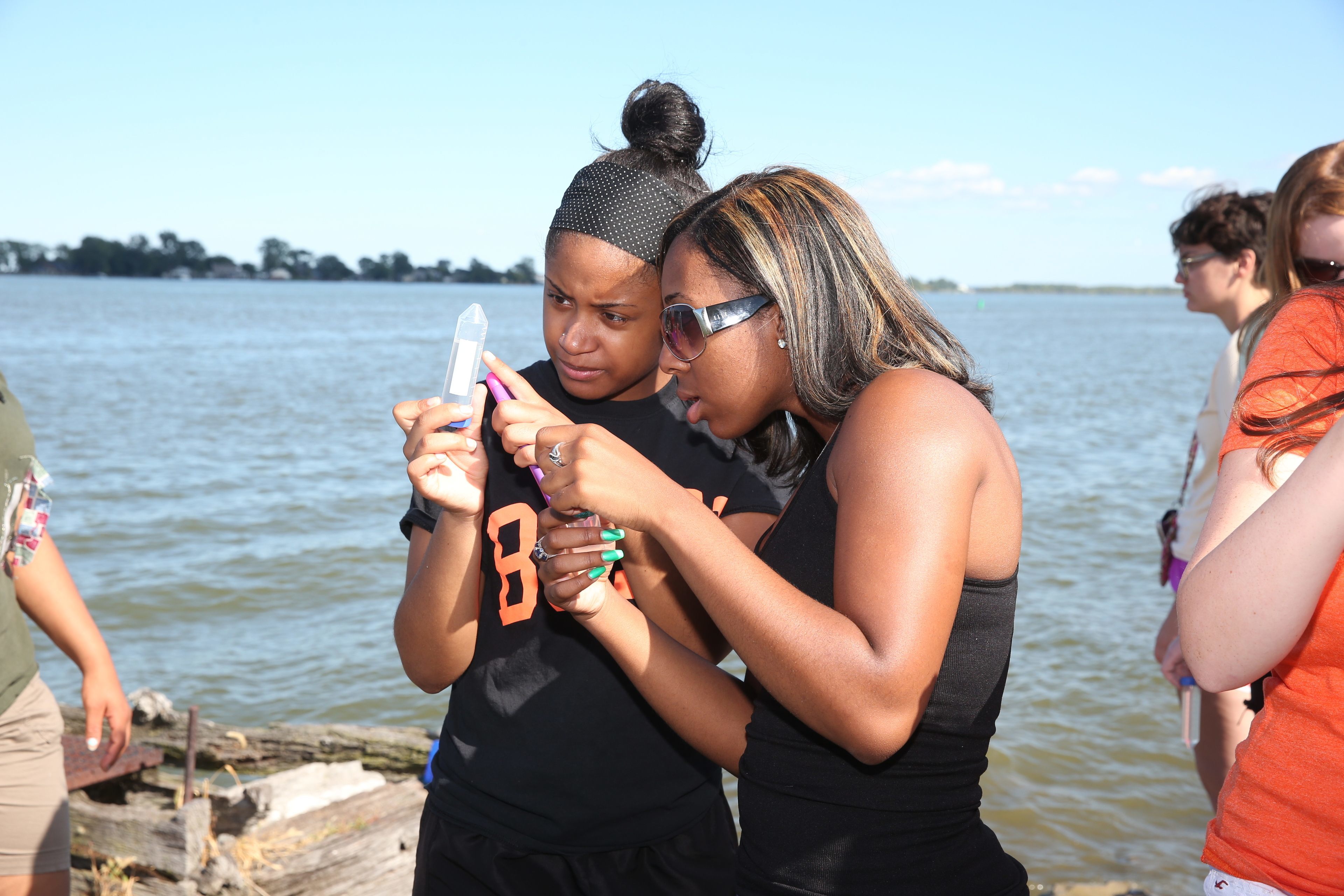 Two people are holding and observing a tube by the ocean