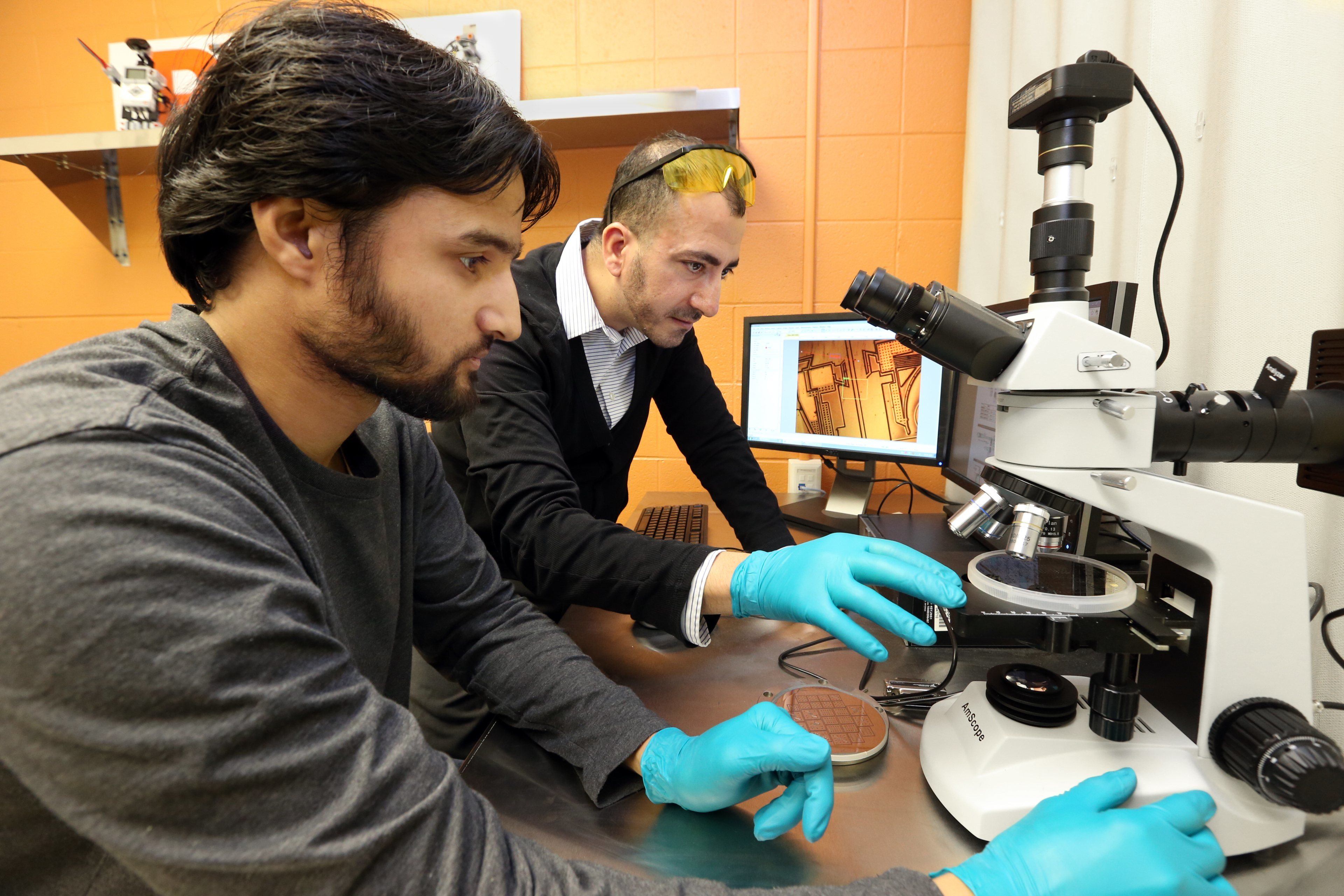A male professor and male BGSU robotics engineering student prepare to use a microscope.