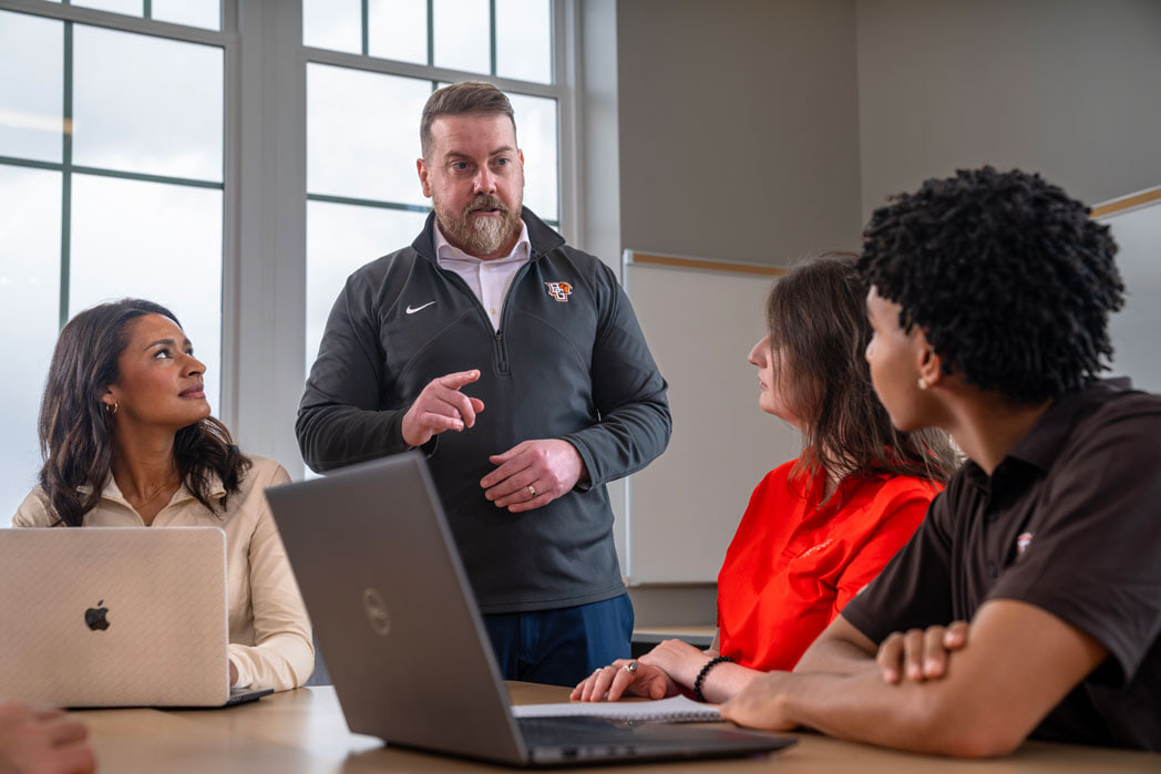Professor speaking to three sitting students.