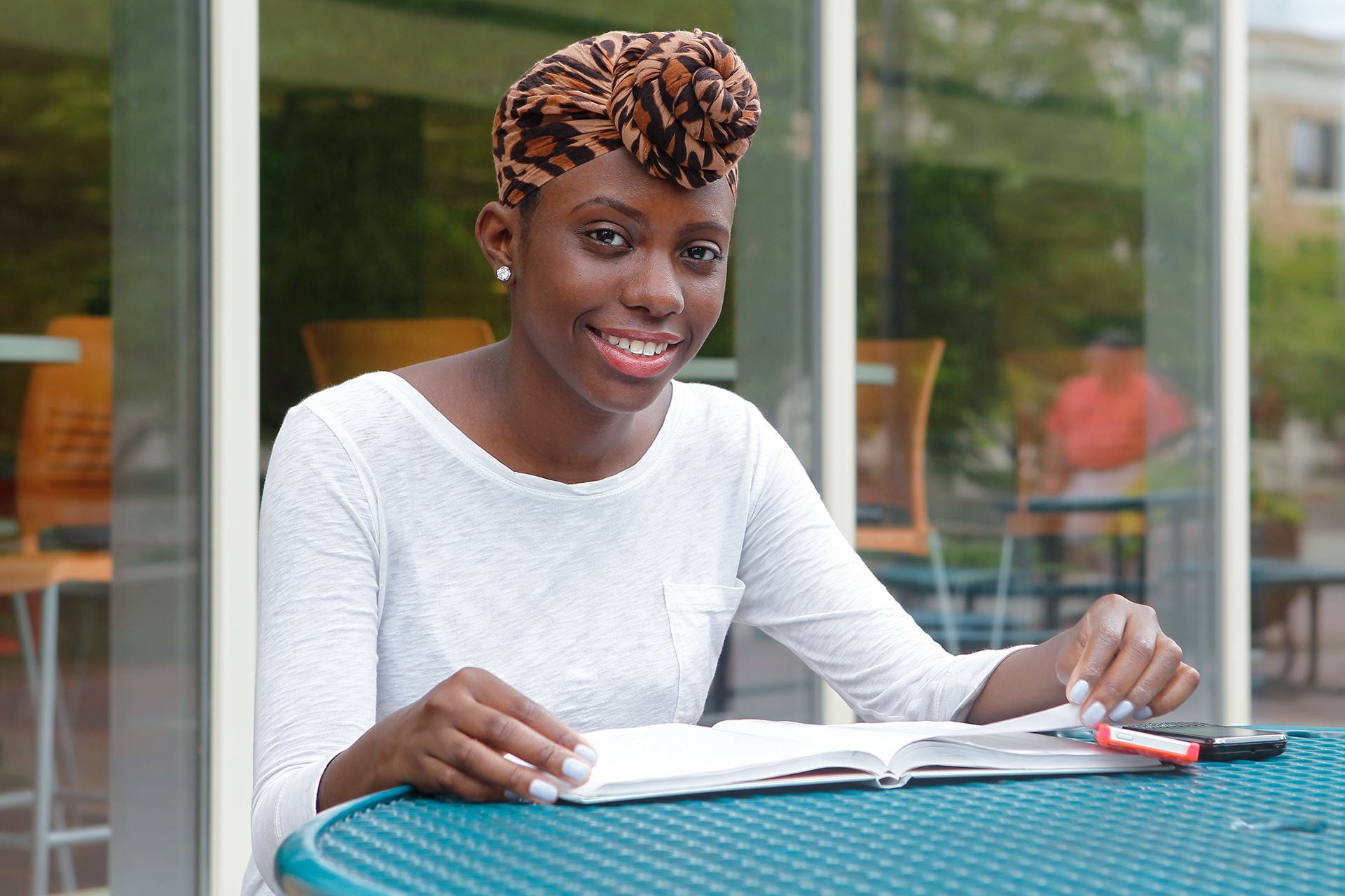 A student sitting outside at a table and smiling at the camera.