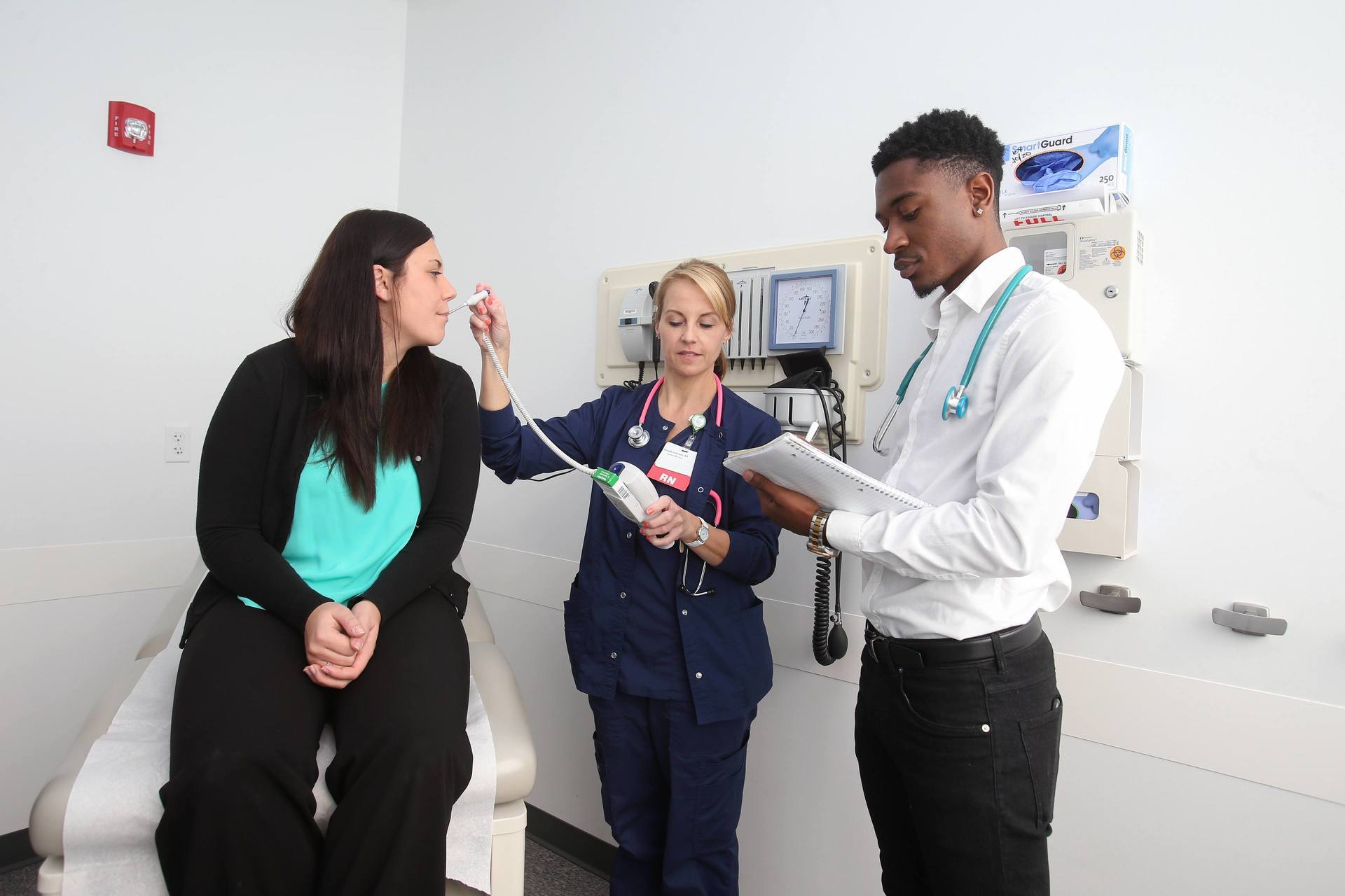 A student watches a nurse take someone's temperature.