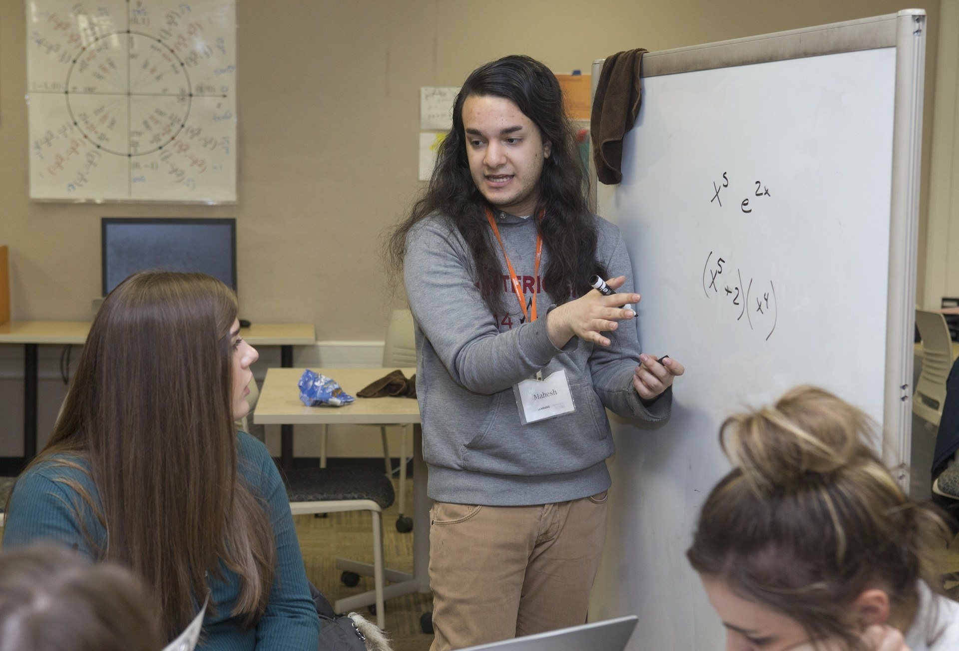 A teacher writing on a dry erase board and talking with a student