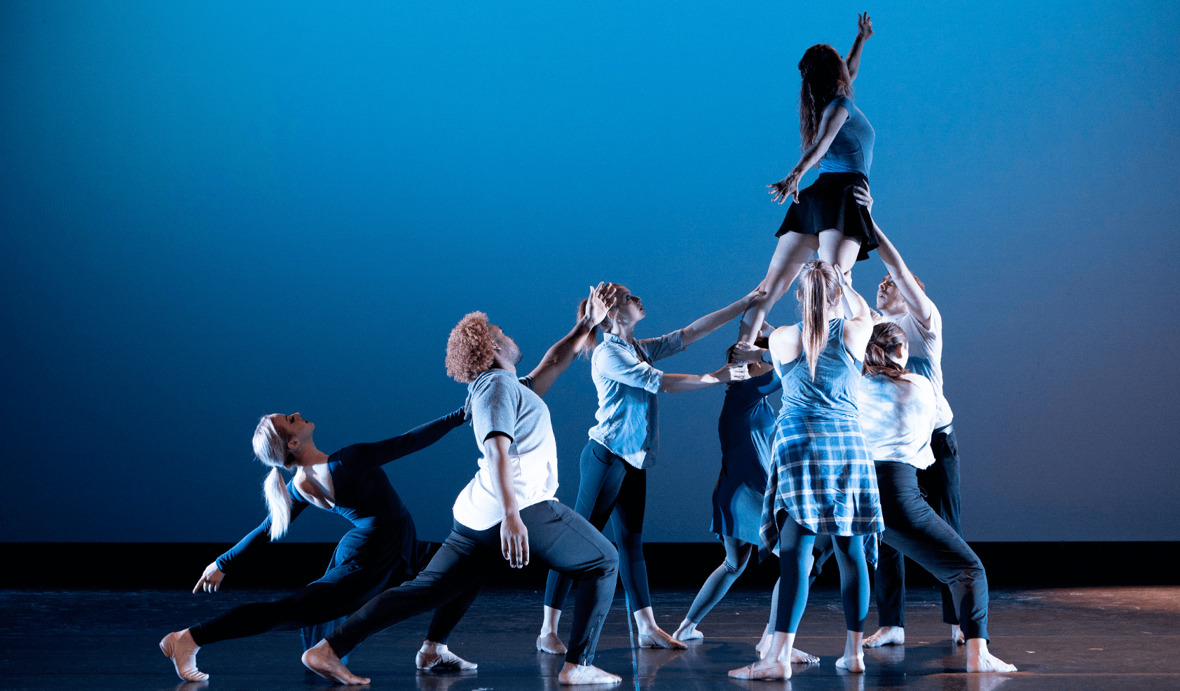 Dancers lift another dancer into the air on a blue background