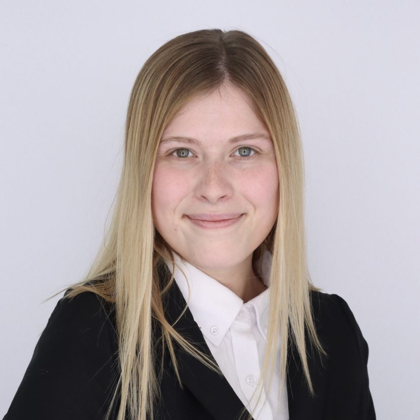 A woman with long blonde hair and a black blaze and a white shirt 