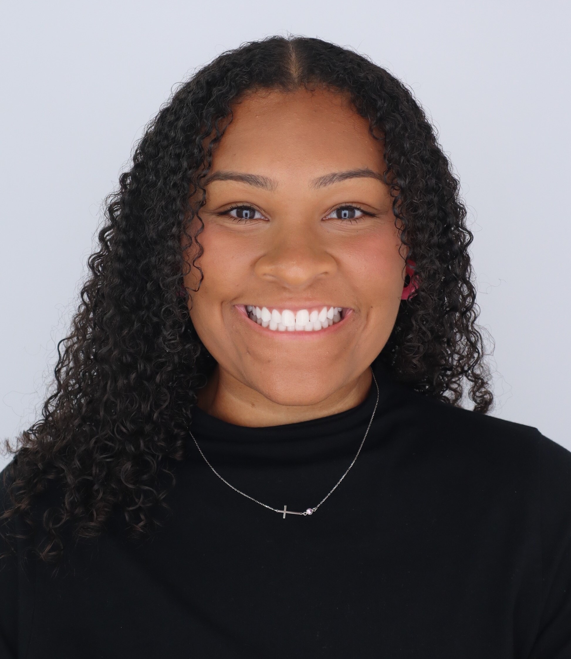 A woman with sholder length curly hair and a peach short sleeve shirt