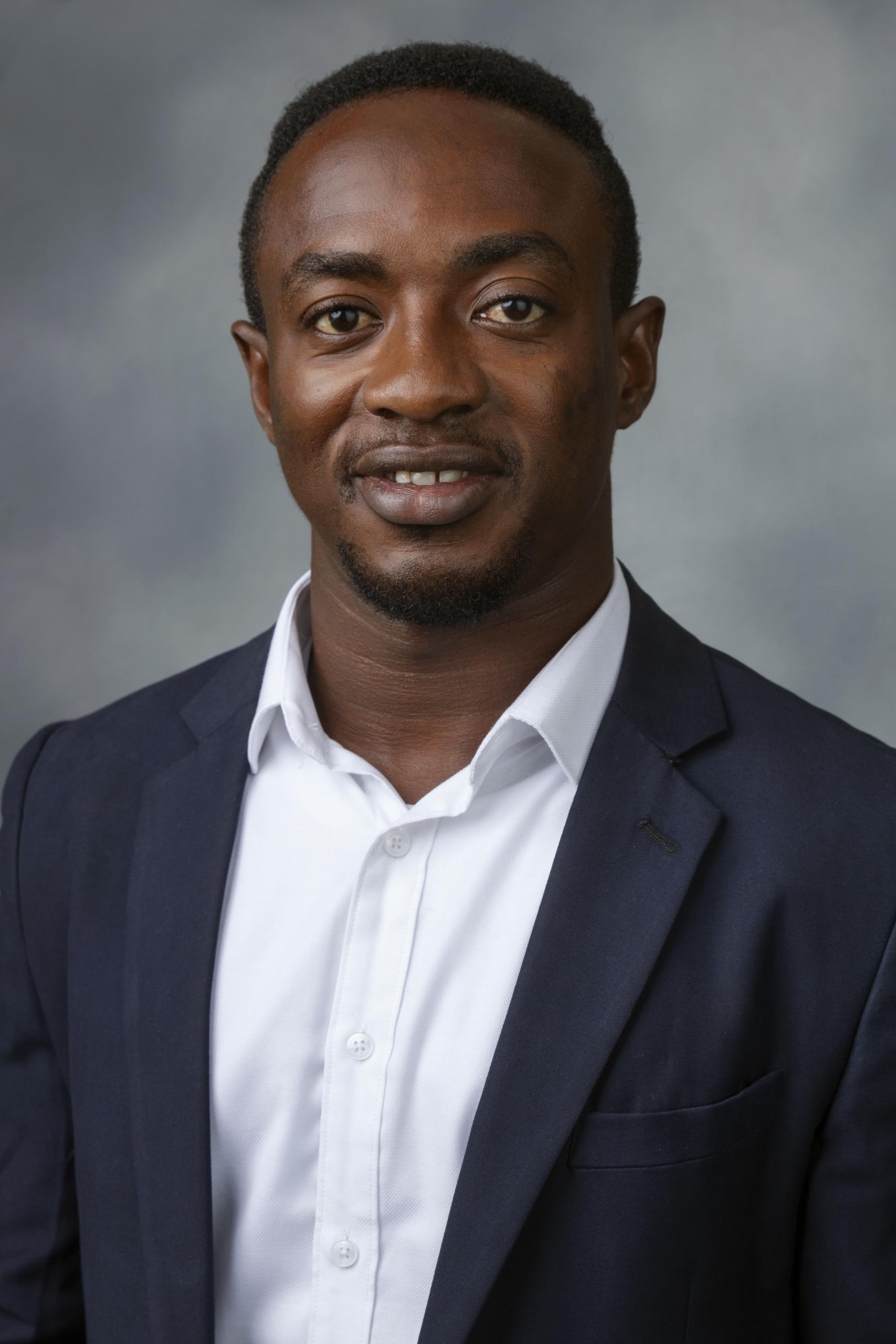 Jon McCullough, in formal attire, in front of gray background.