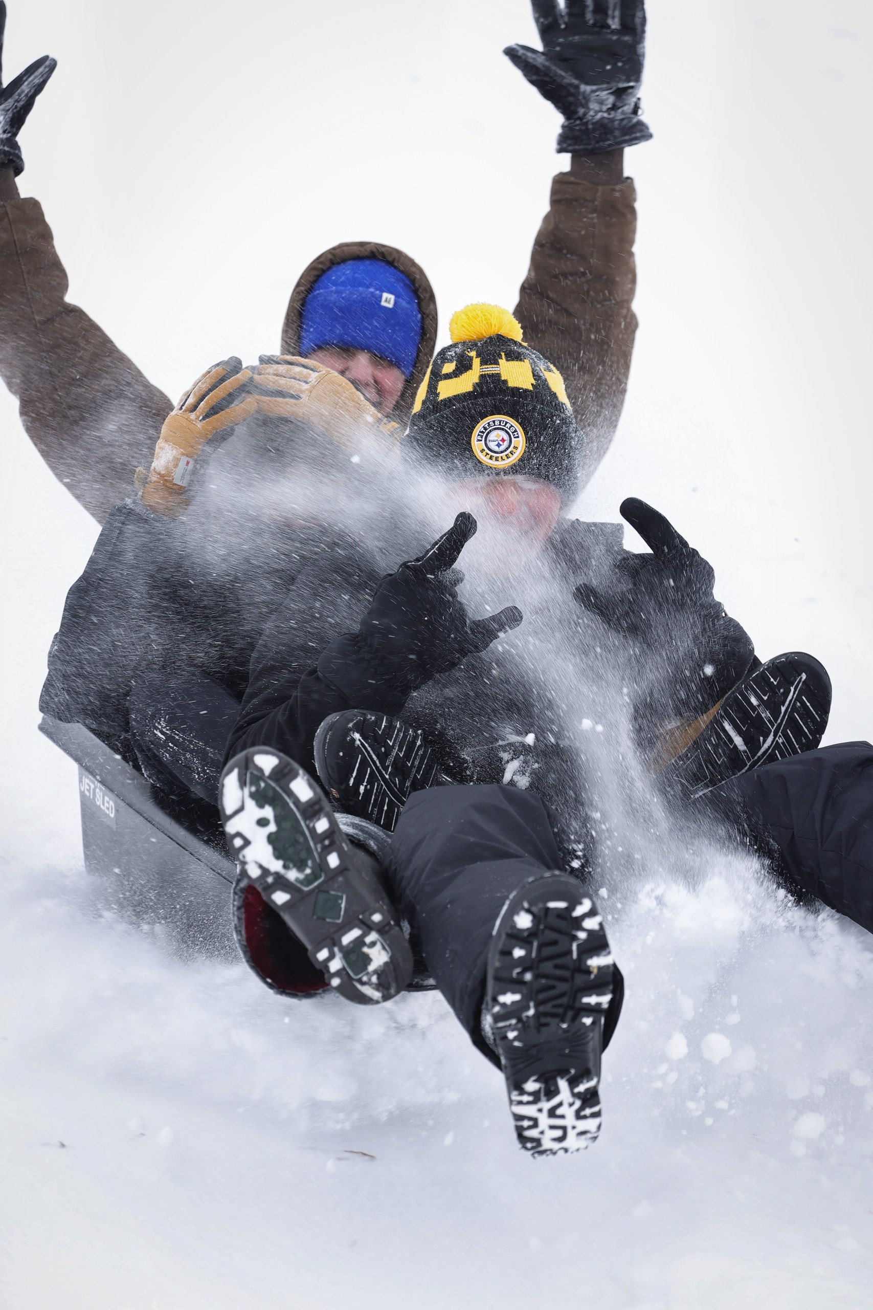 Snow flies in front of three students sledding together. 