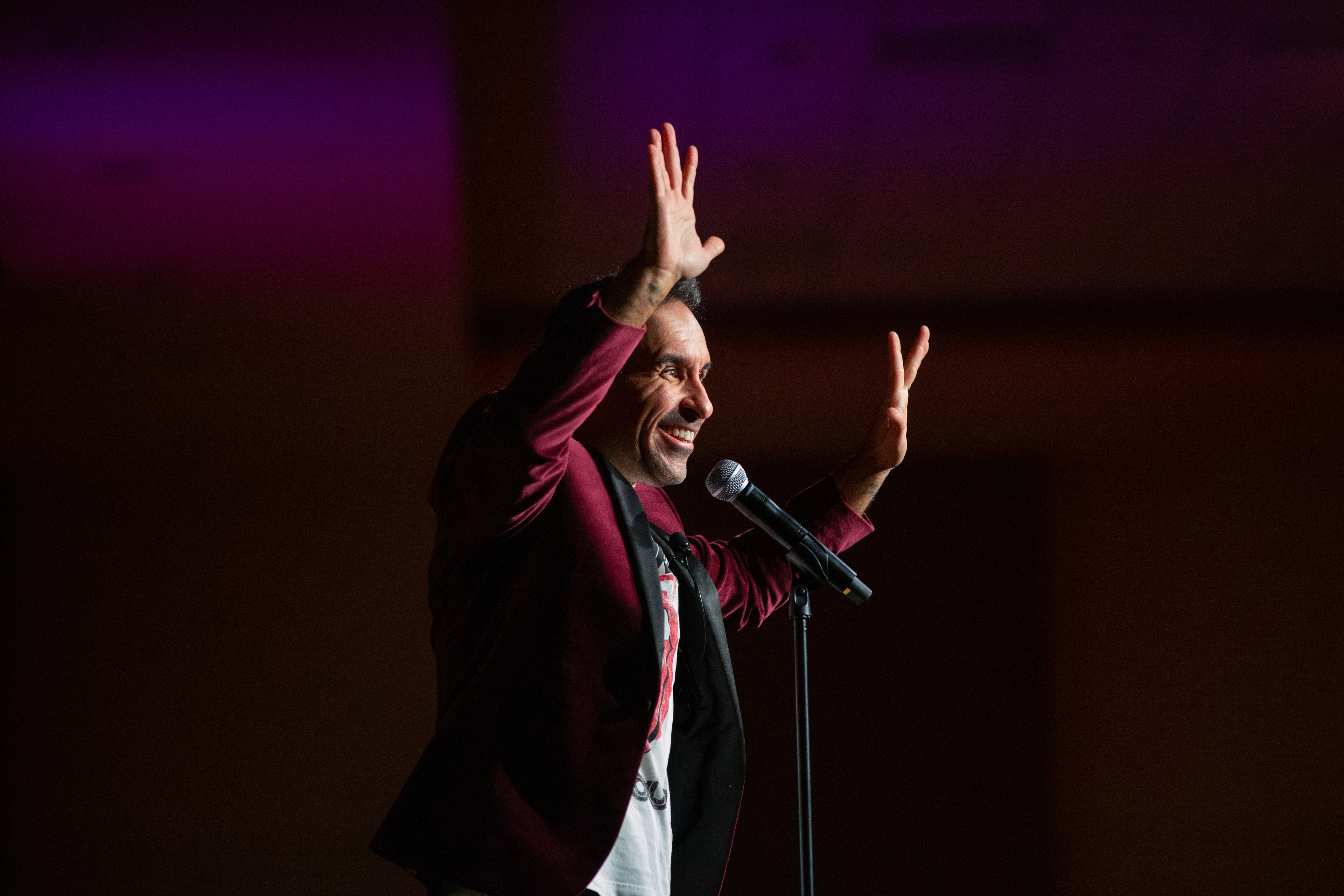 A man raises his hands on stage next to a microphone