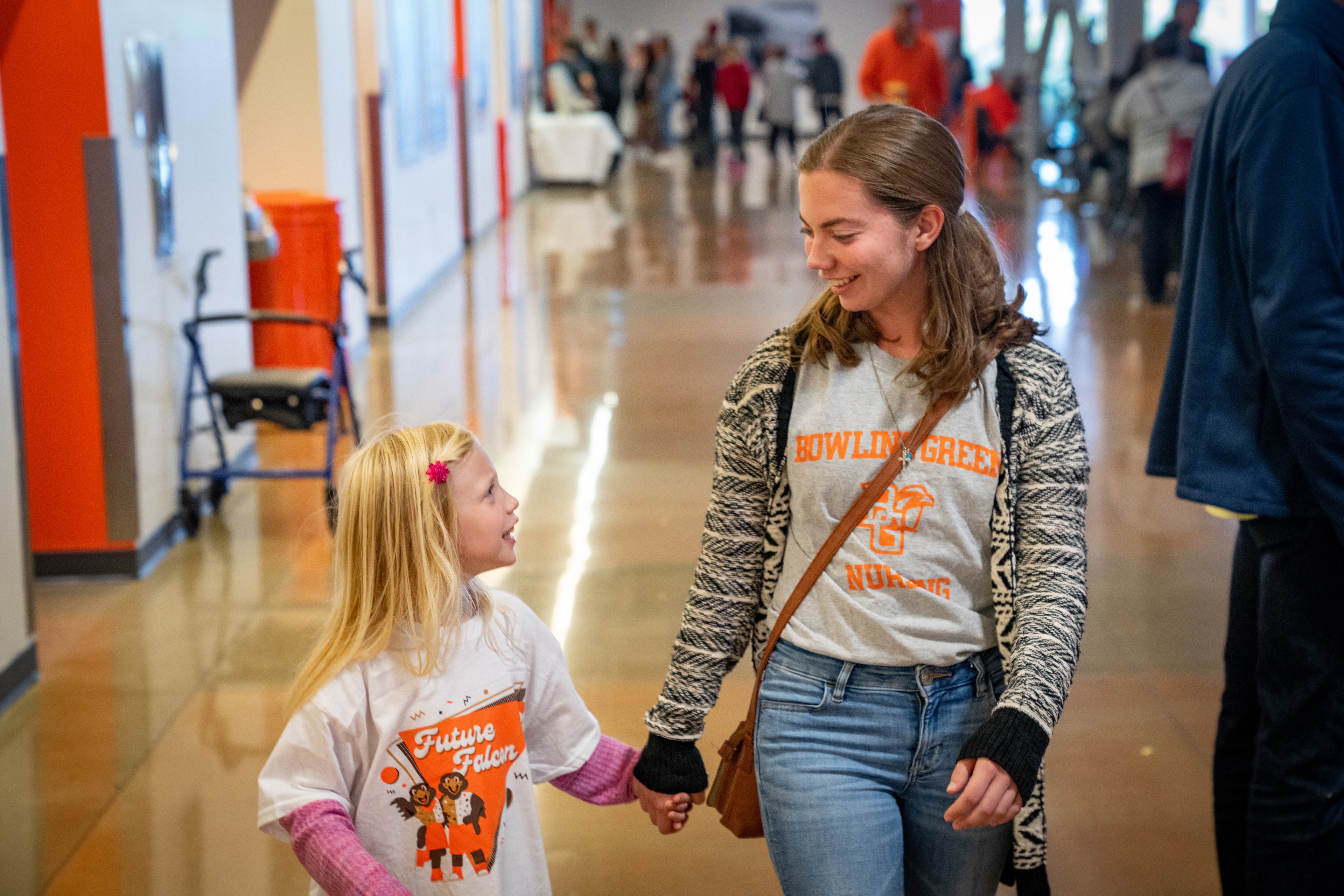 A young woman and a girl hold hands while walking