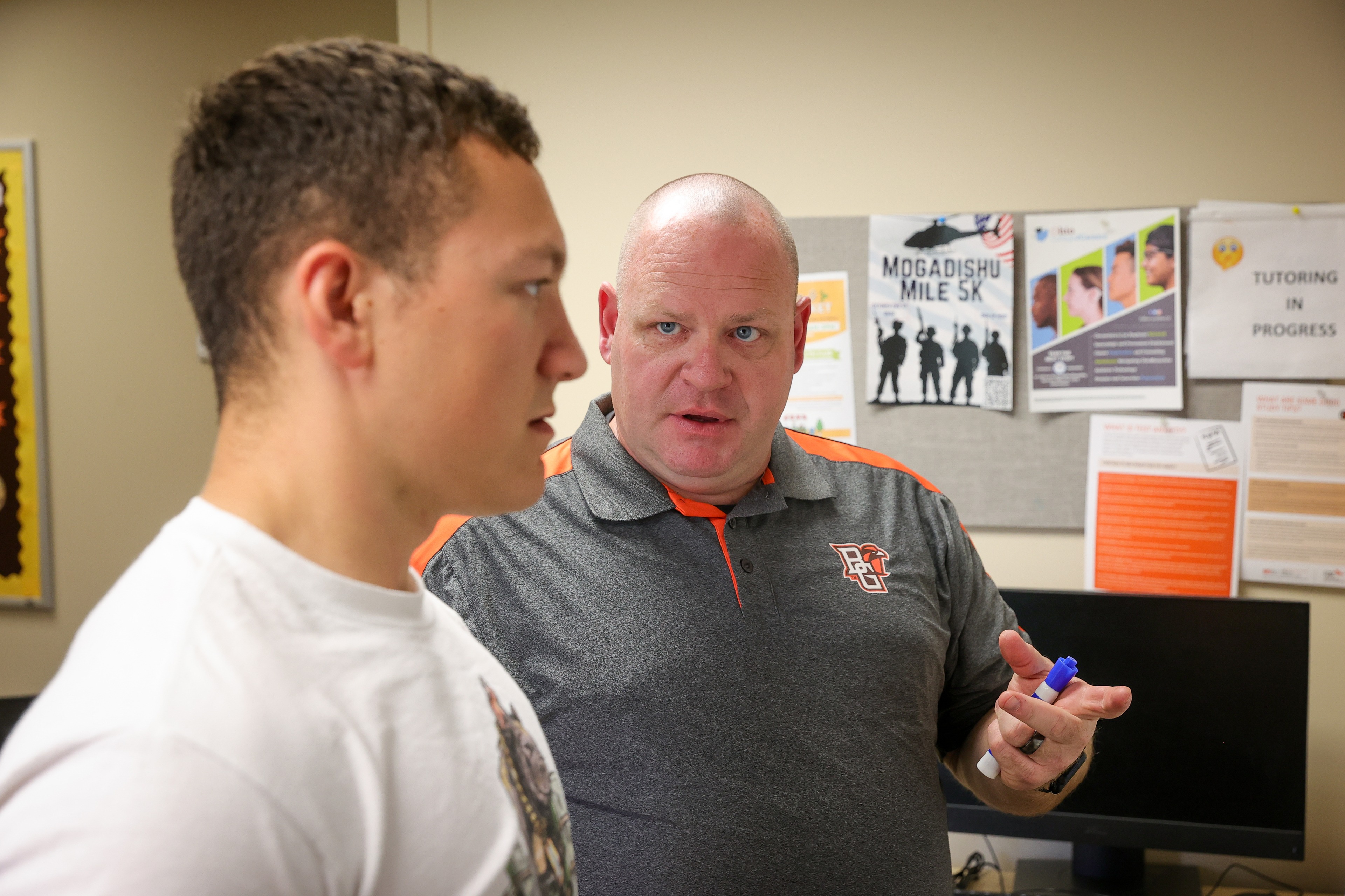 Two men stand before a whiteboard in a classroom 