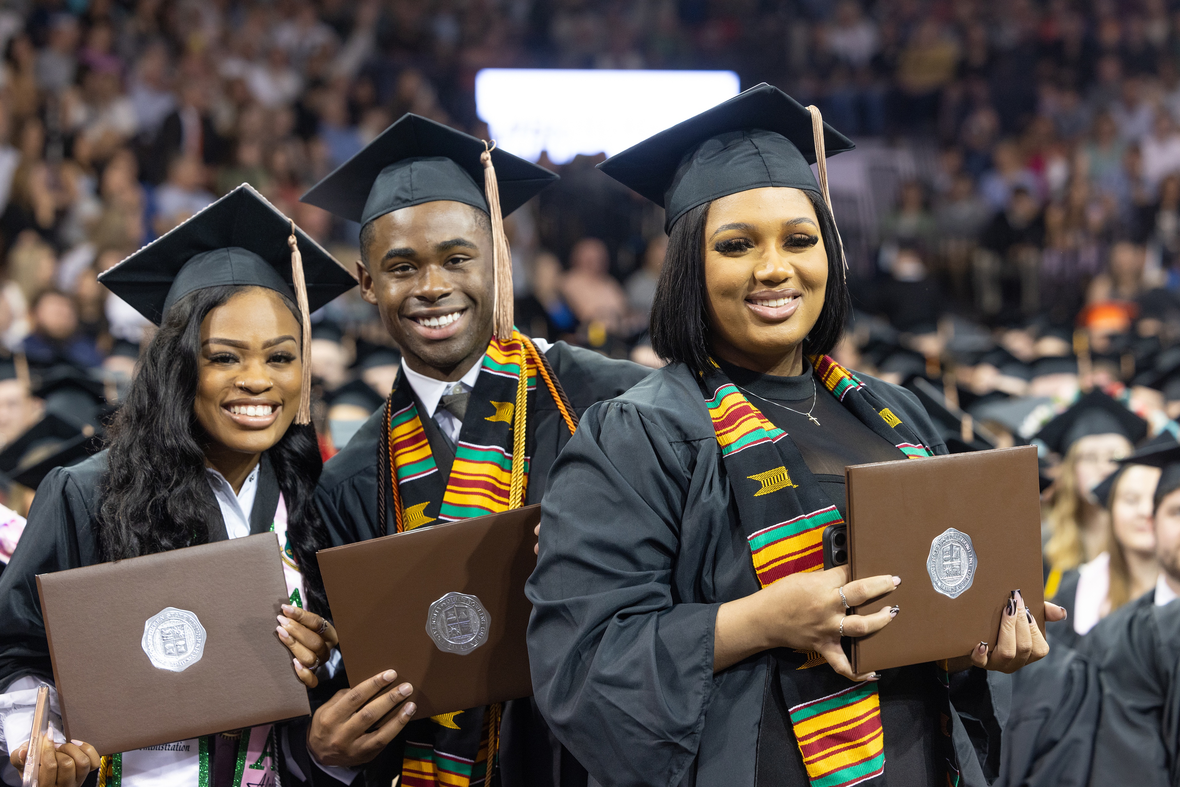 Three graduates hold their diploma covers up
