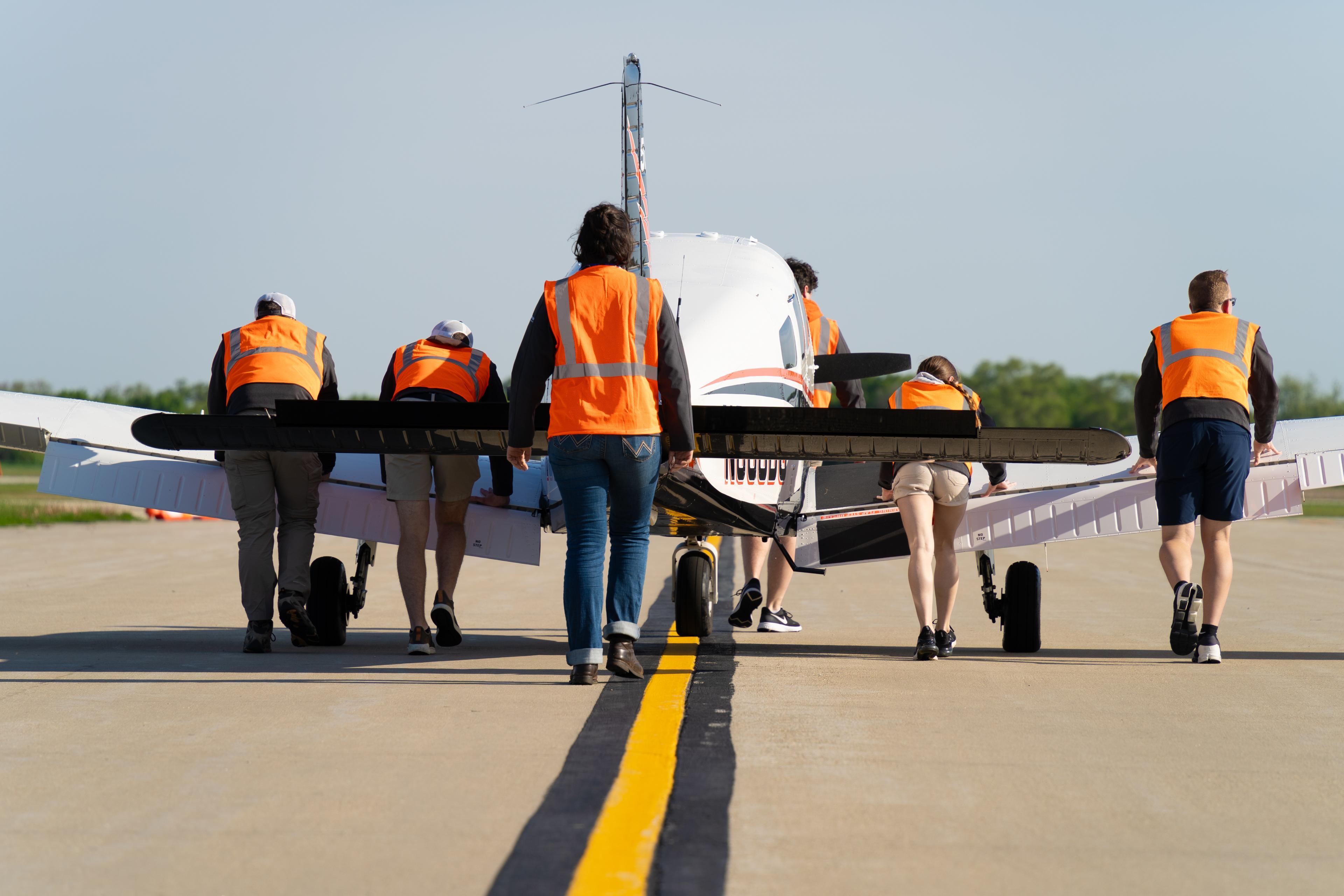People push an airplane down a runway.