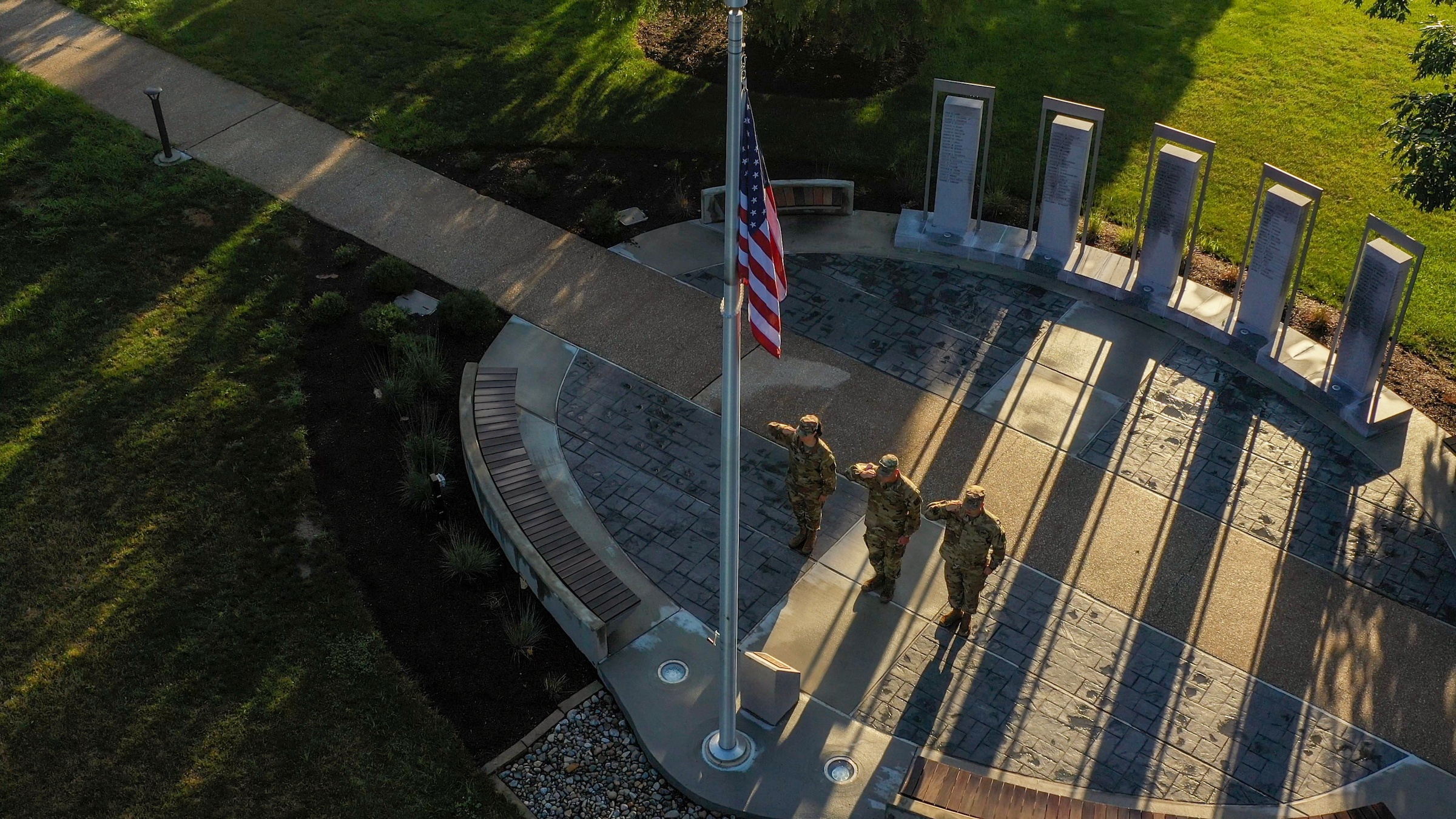 Military members salute the American flag at a veterans memorial.