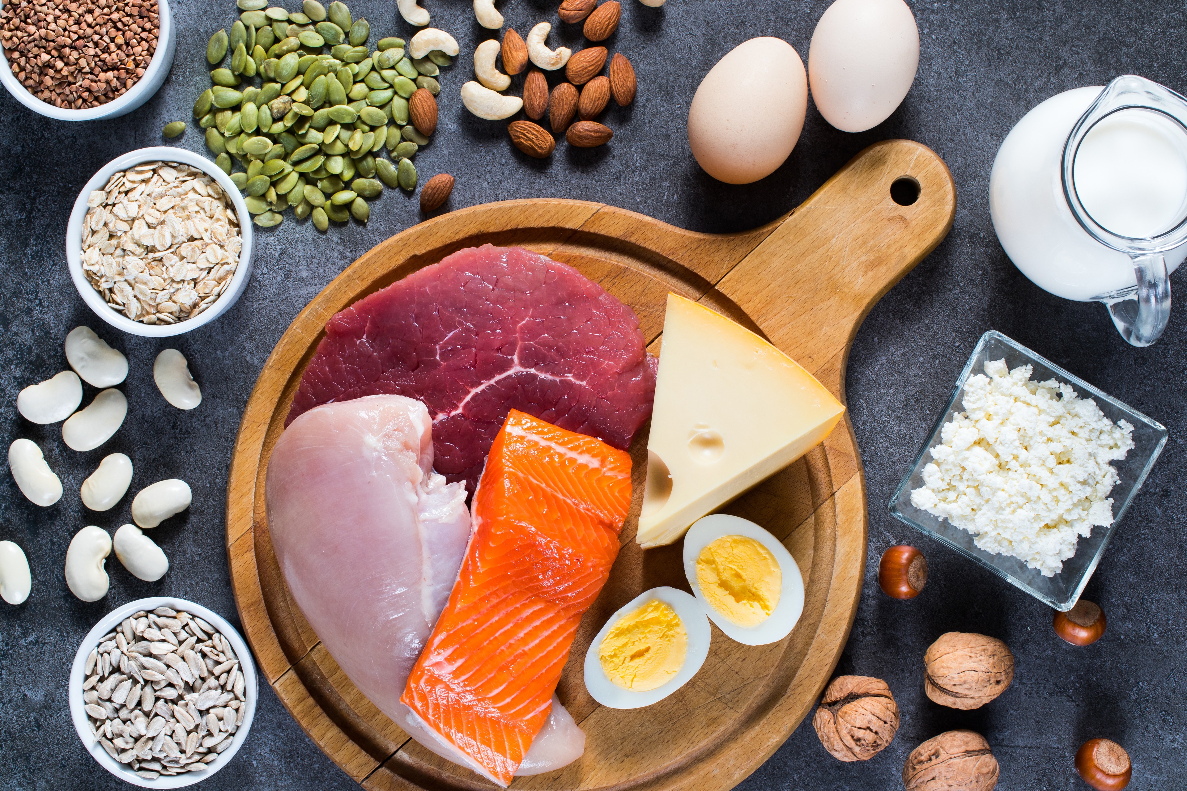 Fish, chicken and beef sit on a cutting board surrounded by nuts, rice, beans and milk