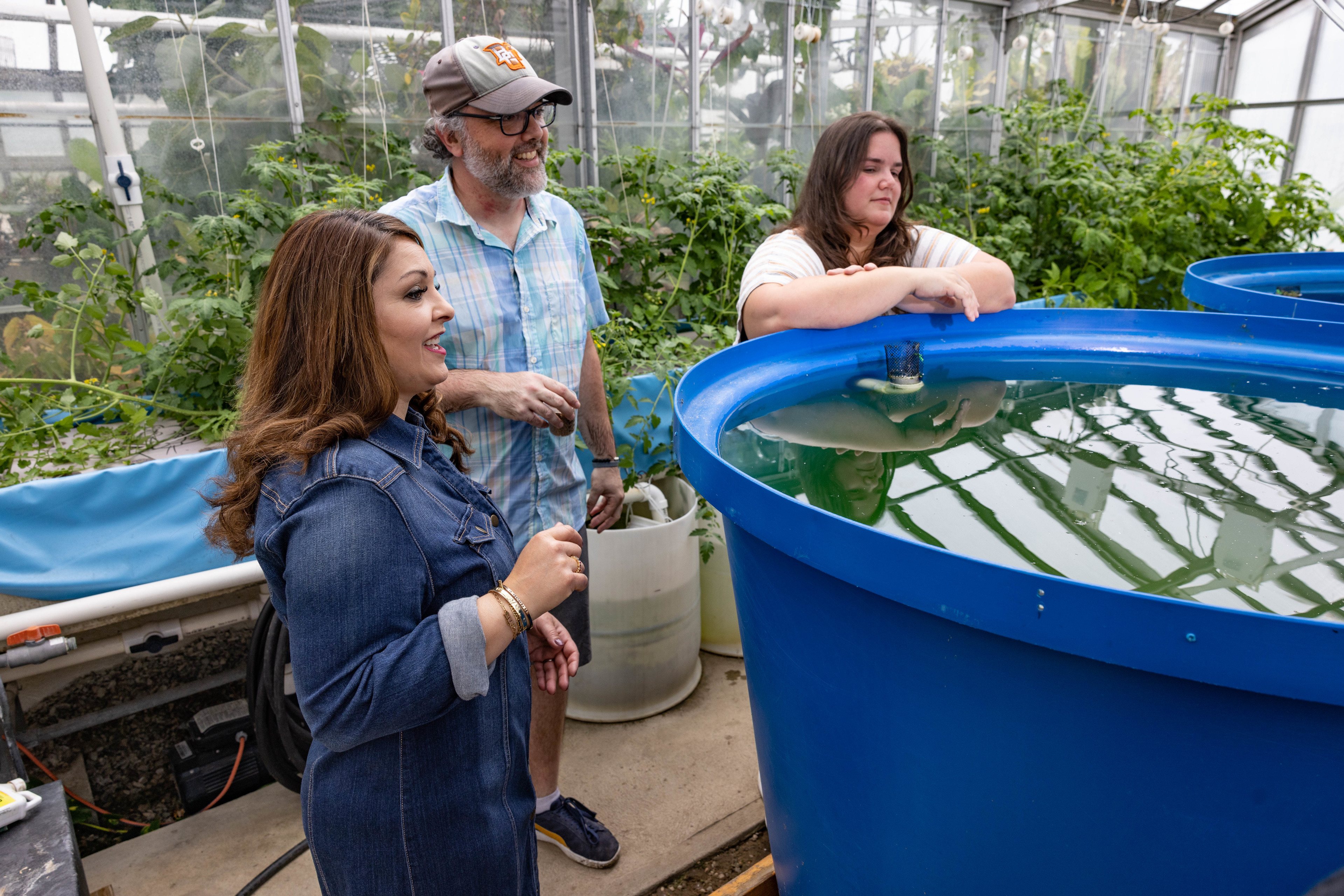 Three people stand around a large blue tank holding crayfish.