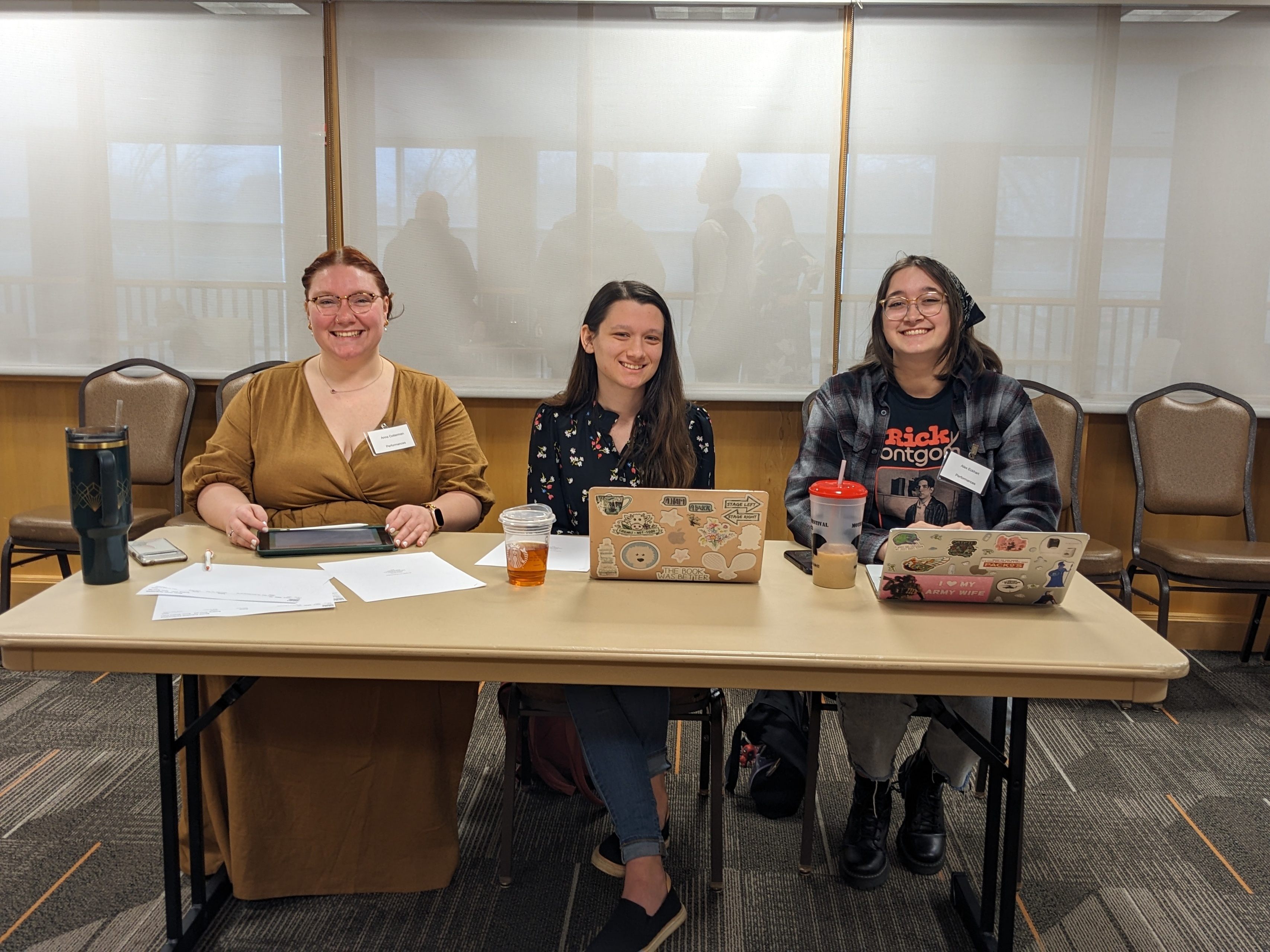 Three people sit at a table with laptops in front of them