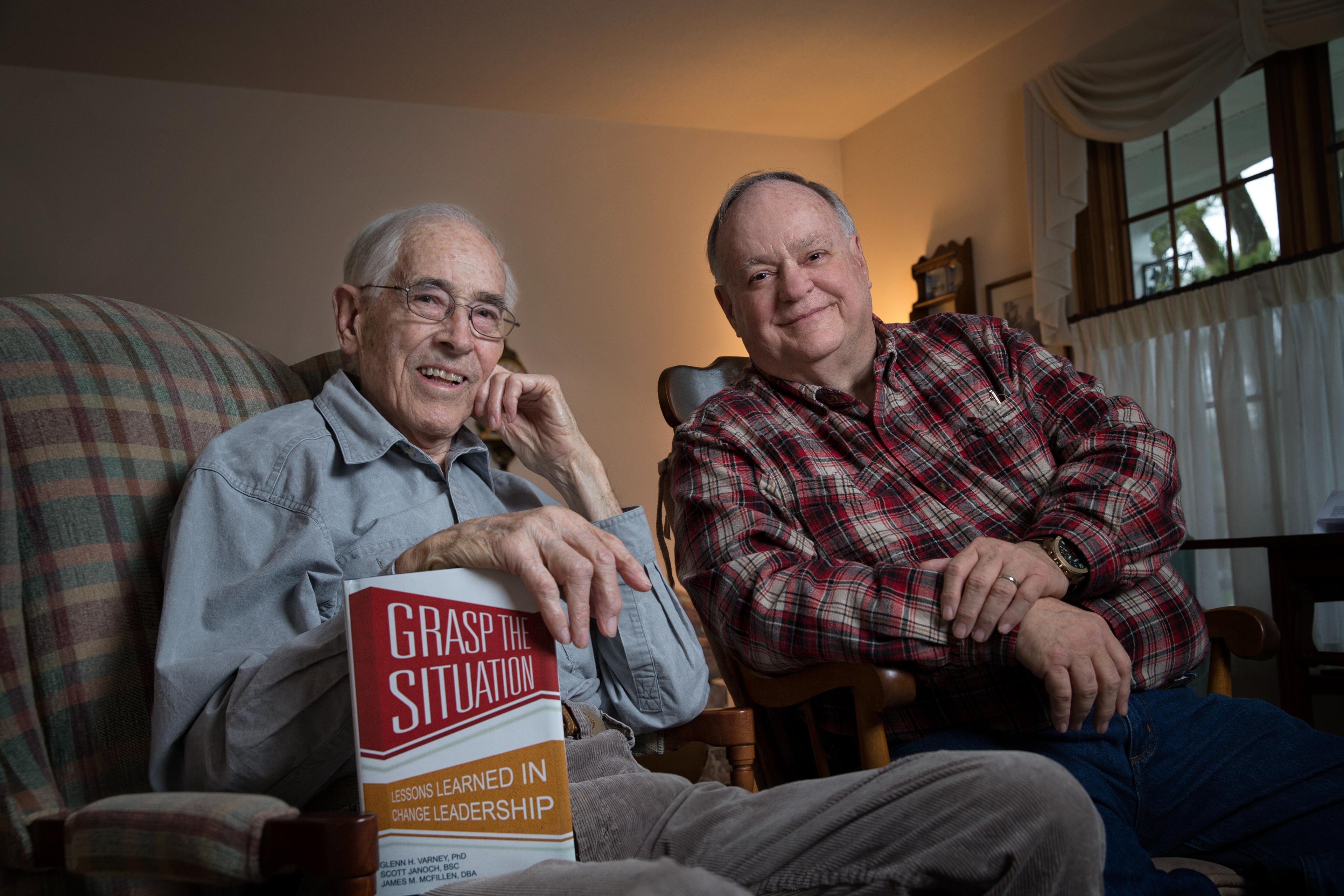 Two people sit on chairs next to each other with a book in the foreground.