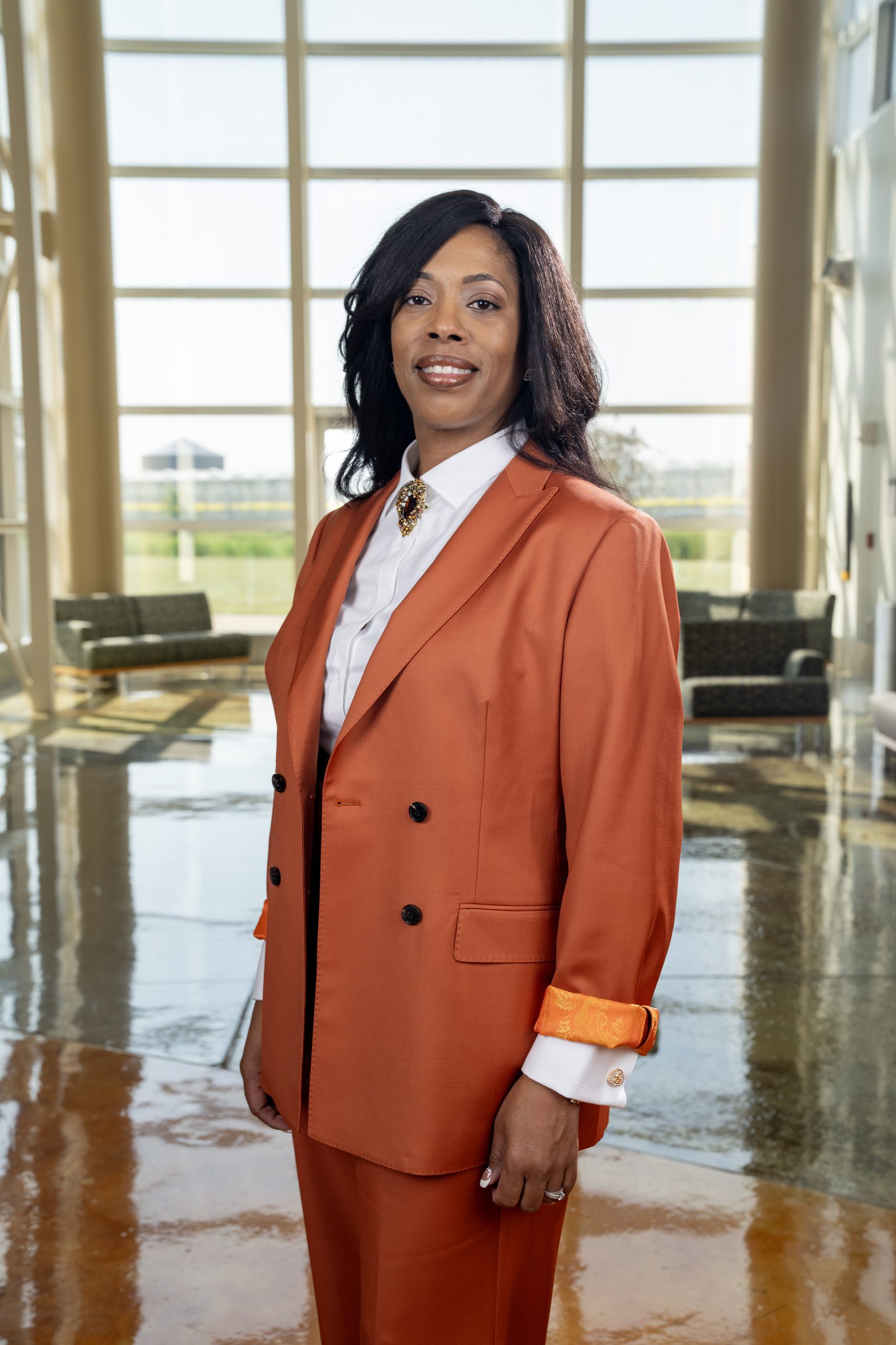 A person wearing an orange business suit stands in an atrium at BGSU Firelands for a photo.