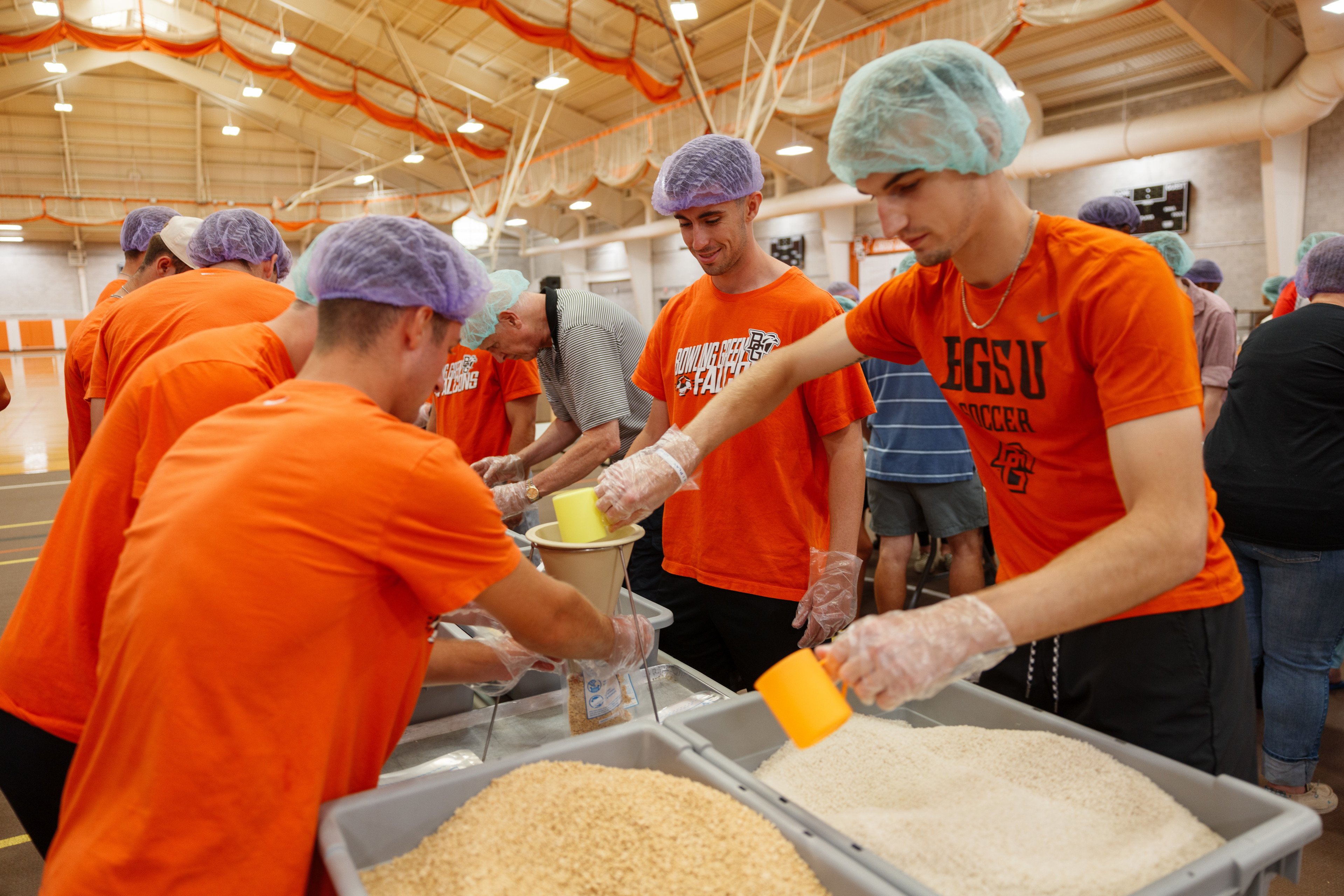 Volunteers in hair nets scoop grains and rice into bags