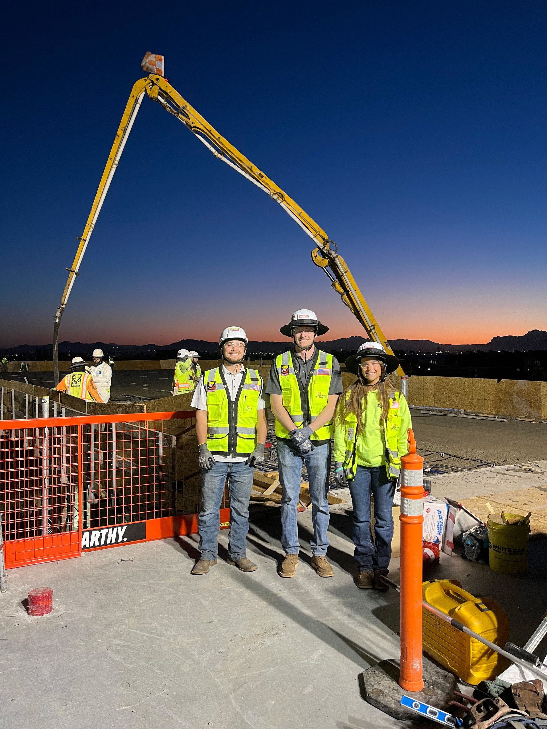 Three construction workers stand on the roof of a construction site at dawn