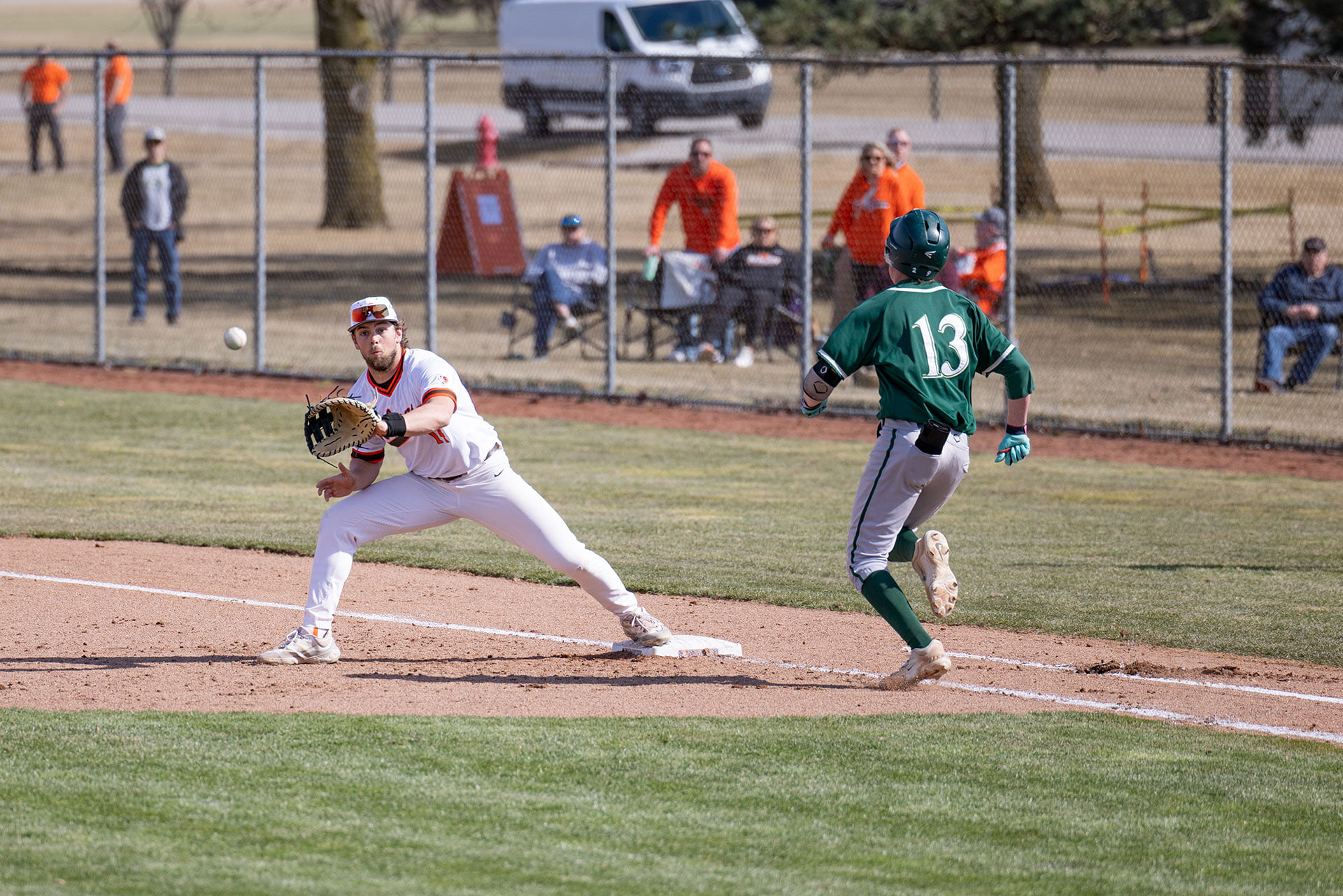 A person prepares to catch a ball at first base as a runner approaches.