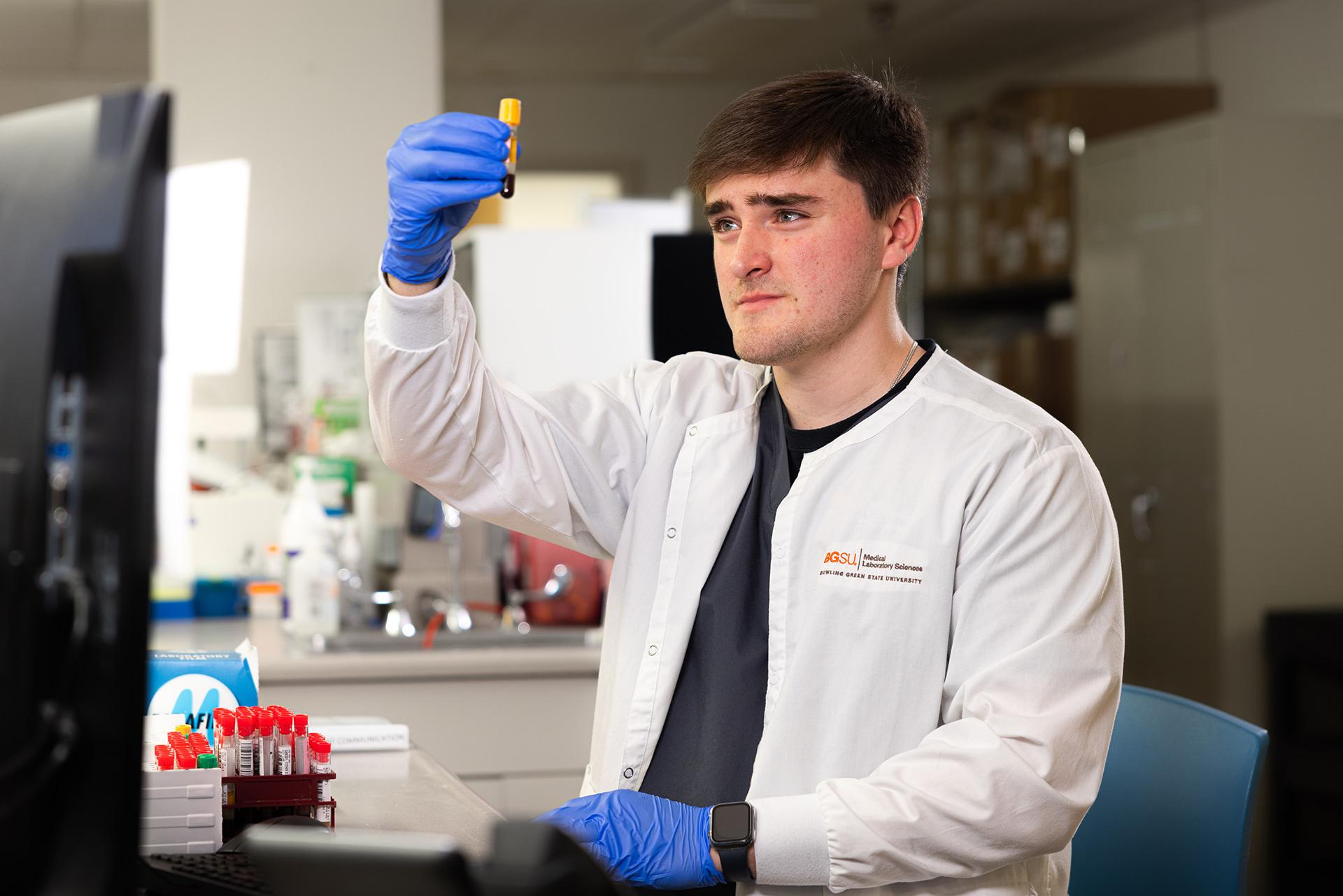 A person in a lab coat looks at a vial of blood