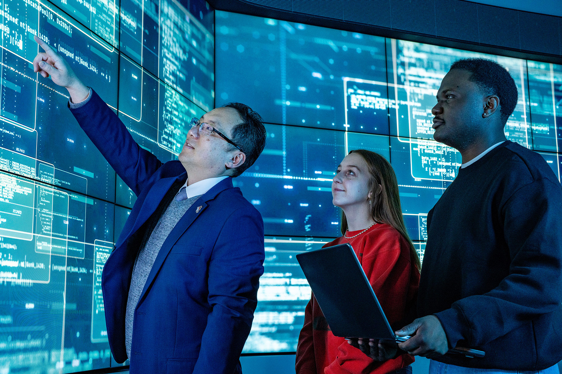 Three people look at floor to ceiling data screens