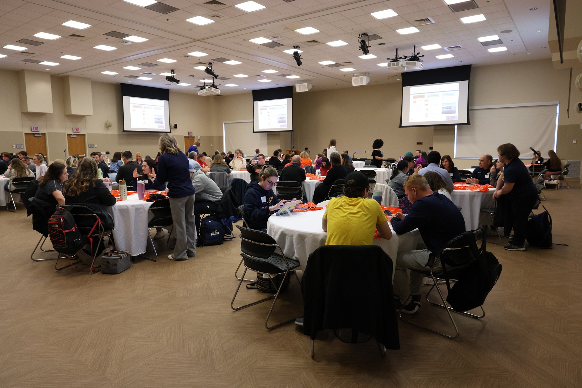 Wide shot of people sitting at tables in front of a projection screnn