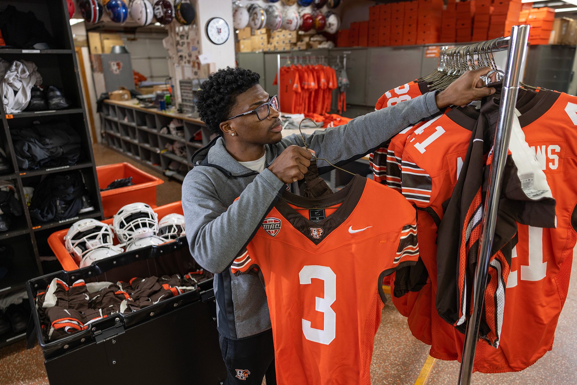 A person puts football jerseys on a hanger.