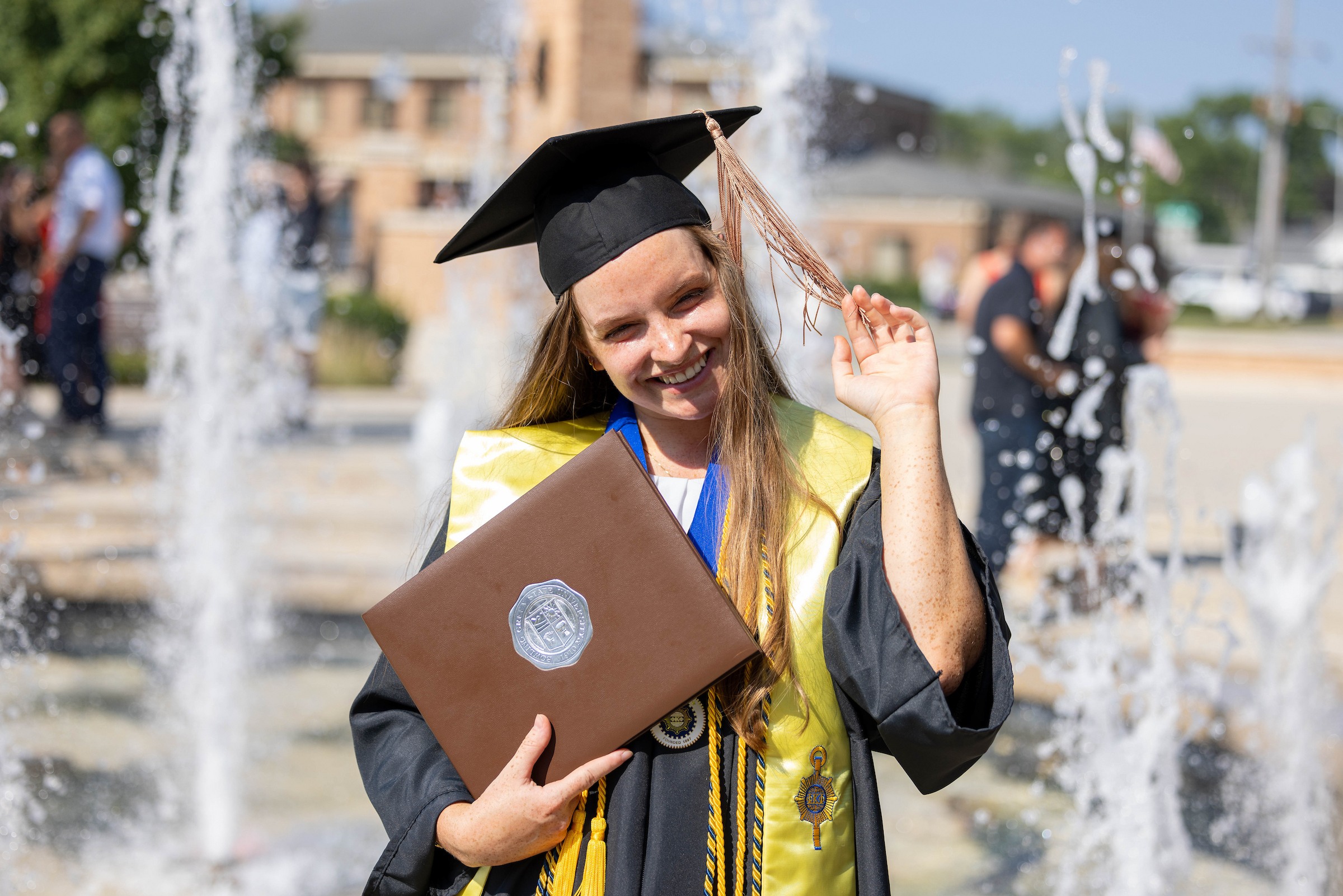 A BGSU graduate in front of the fountain at Alumni Gateway