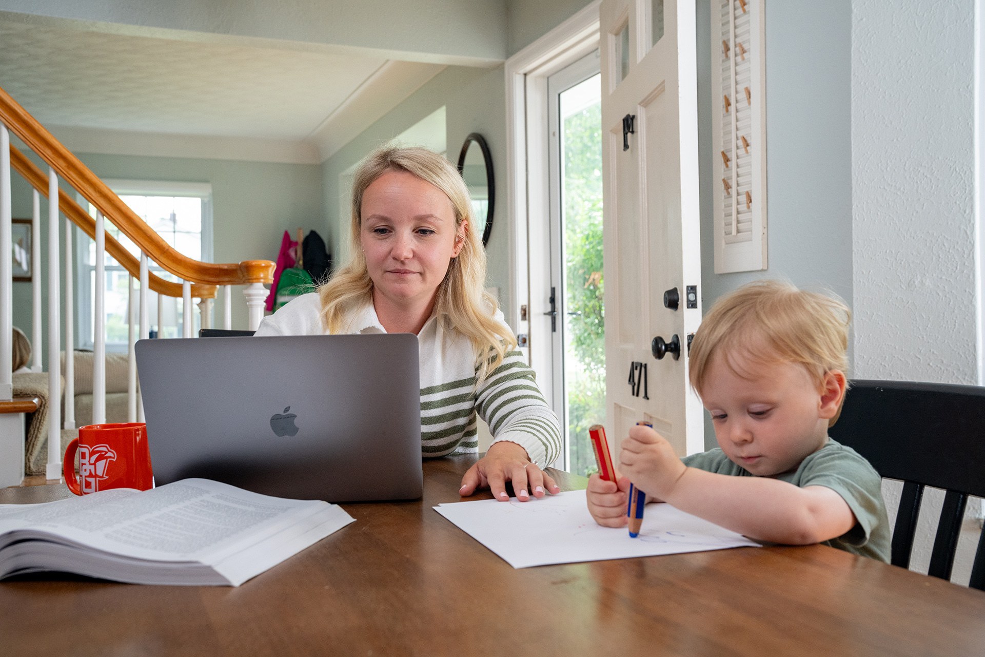 A person works on a laptop with a child nearby.