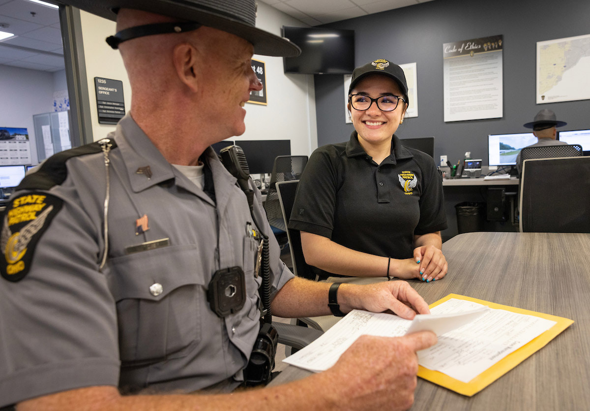 Two people talk at a desk.