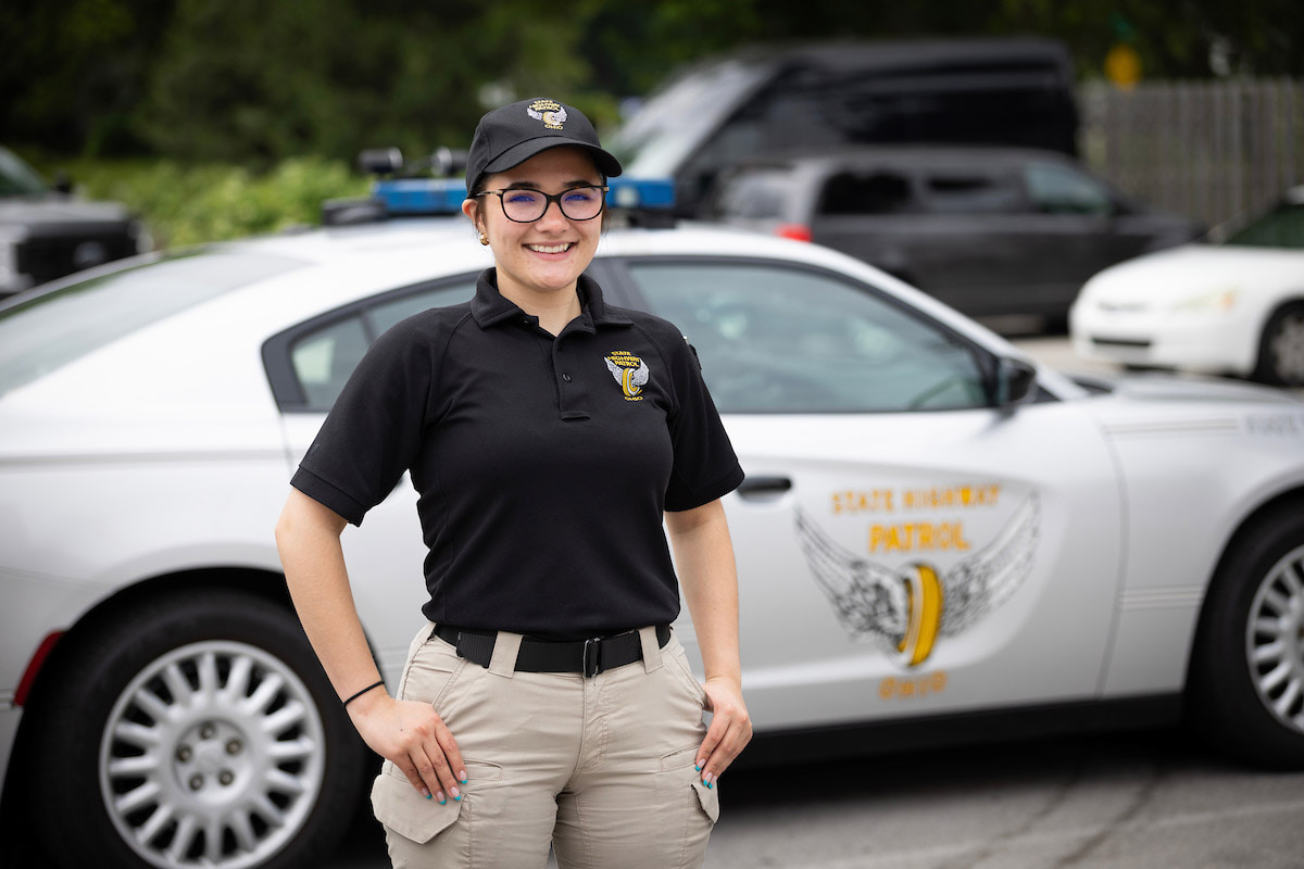 A person stands in front of a police cruiser.