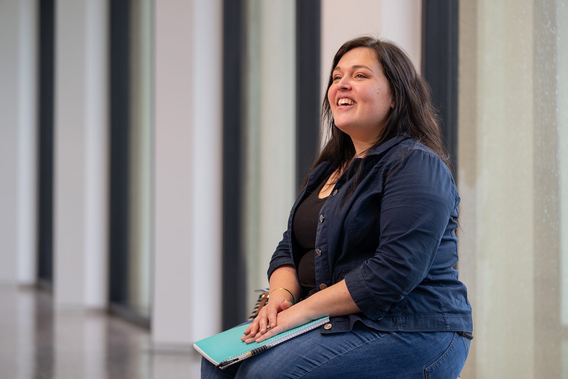 BGSU Firelands student Catalina Ari smiles sitting on a bench on campus while holding a blue notebook.