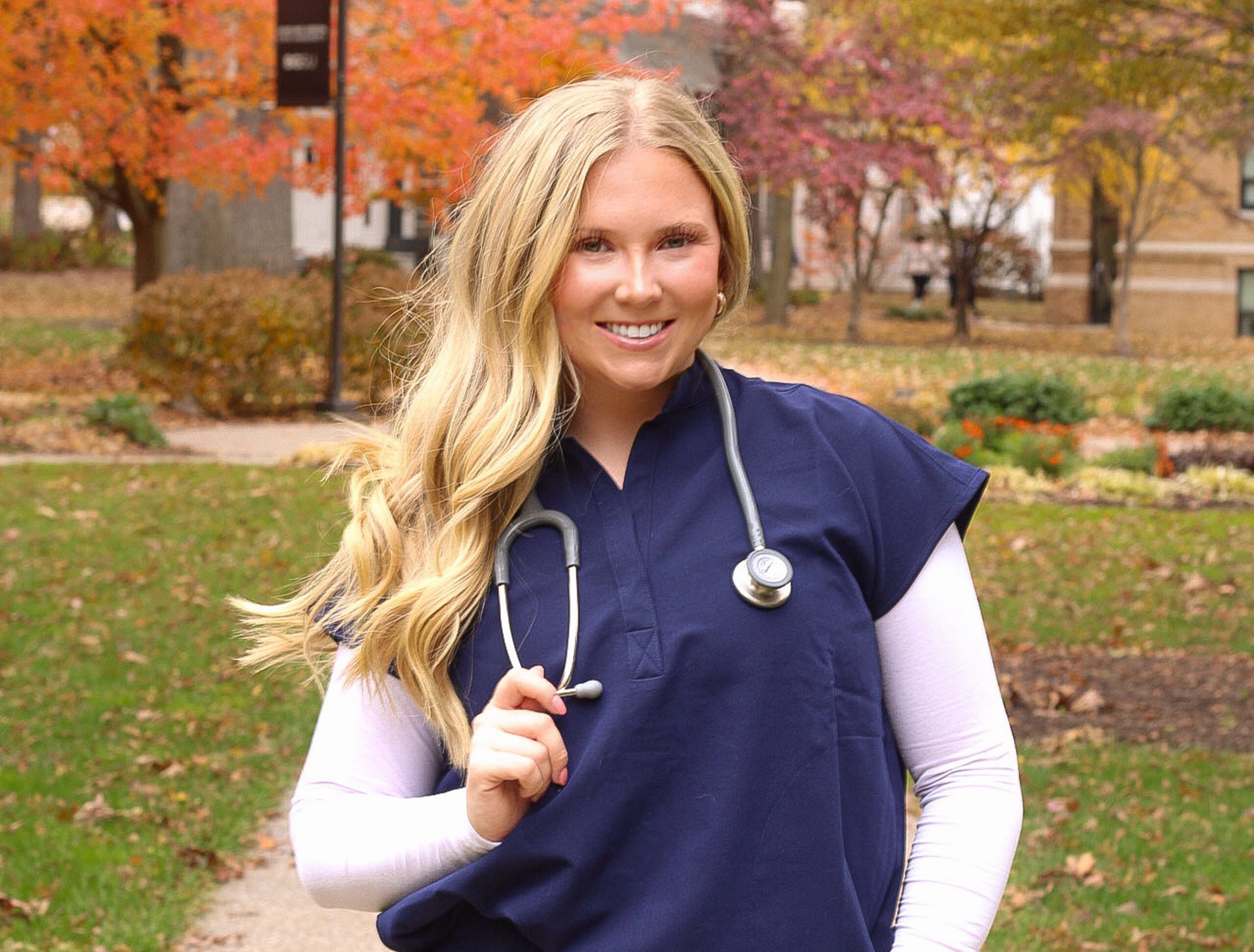 A person wearing blue nursing scrubs poses for a photo on the BGSU campus