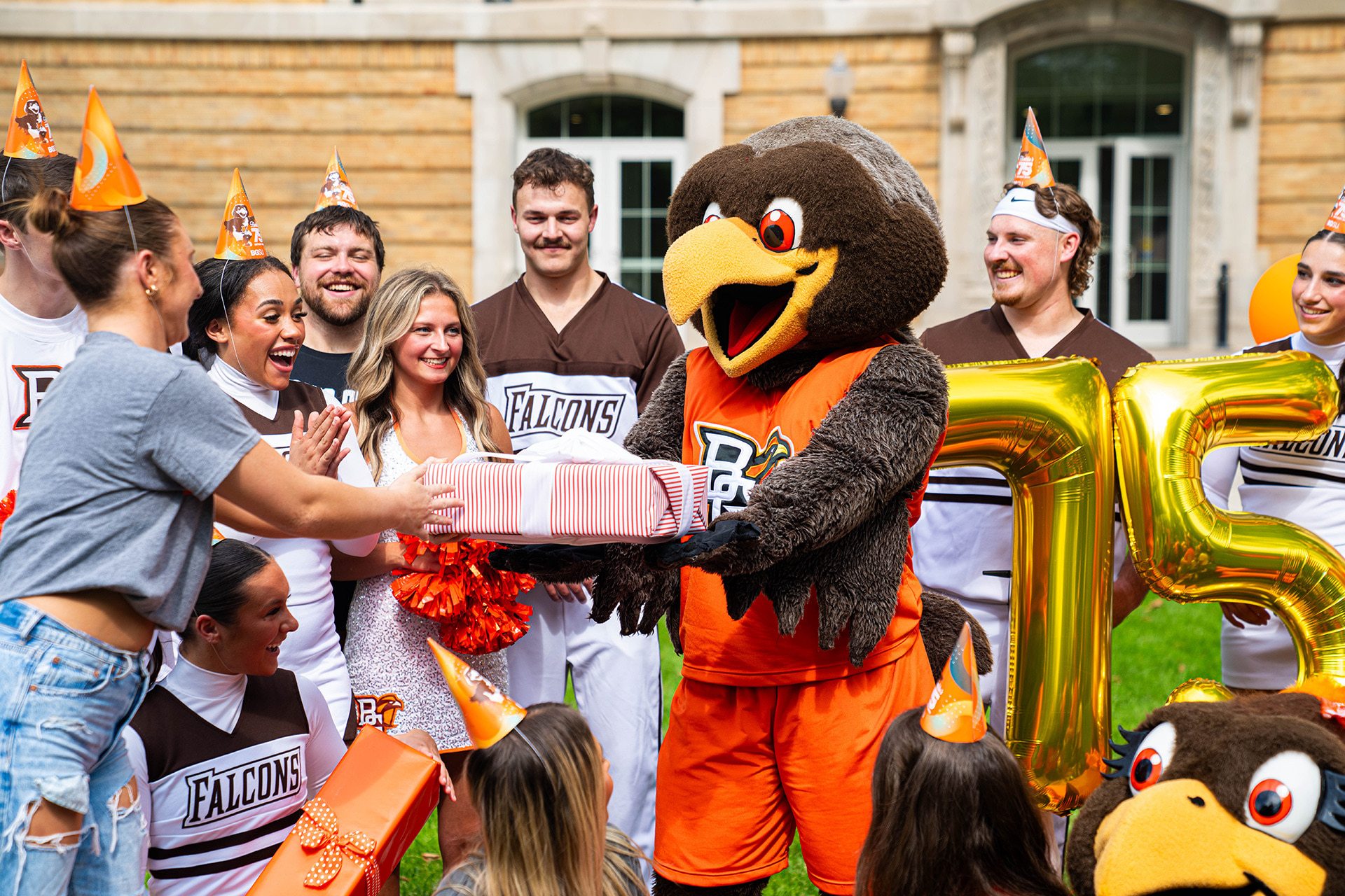A falcon mascot holds a present surrounded by people