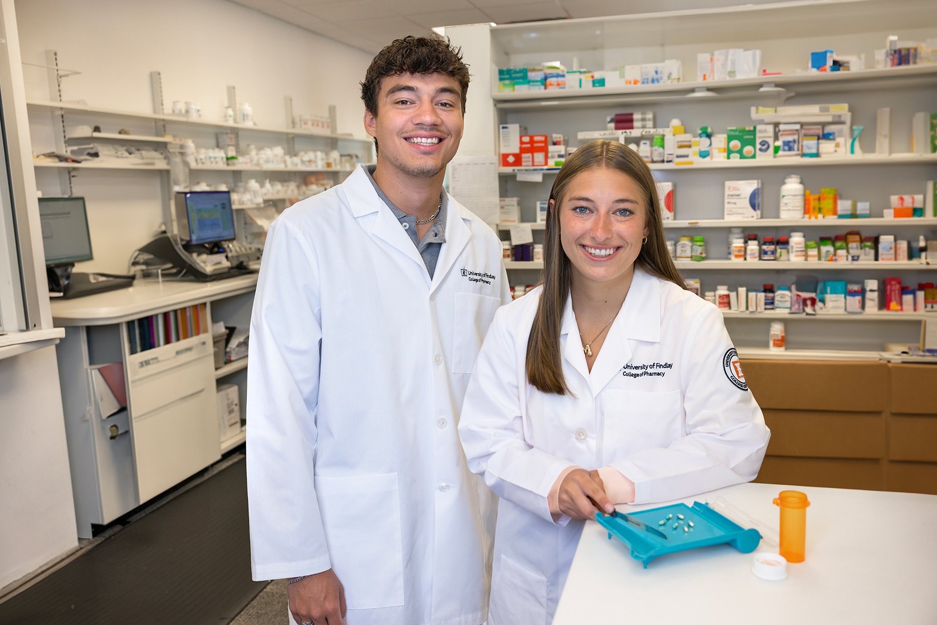 Two people wearing white medical coats stand in a pharmacy