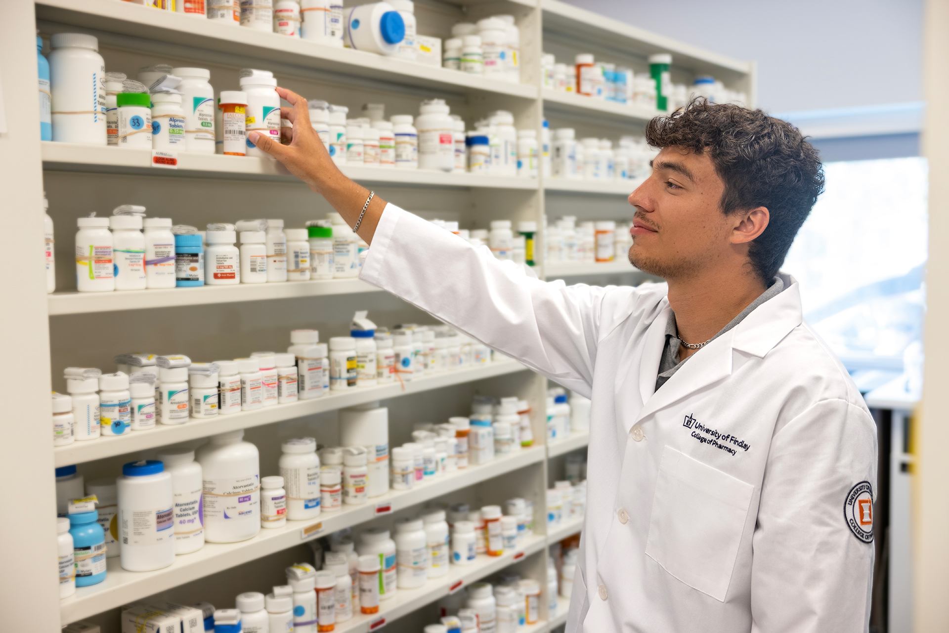 A pharmacist reaches for a bottle of medicine in a pharmacy