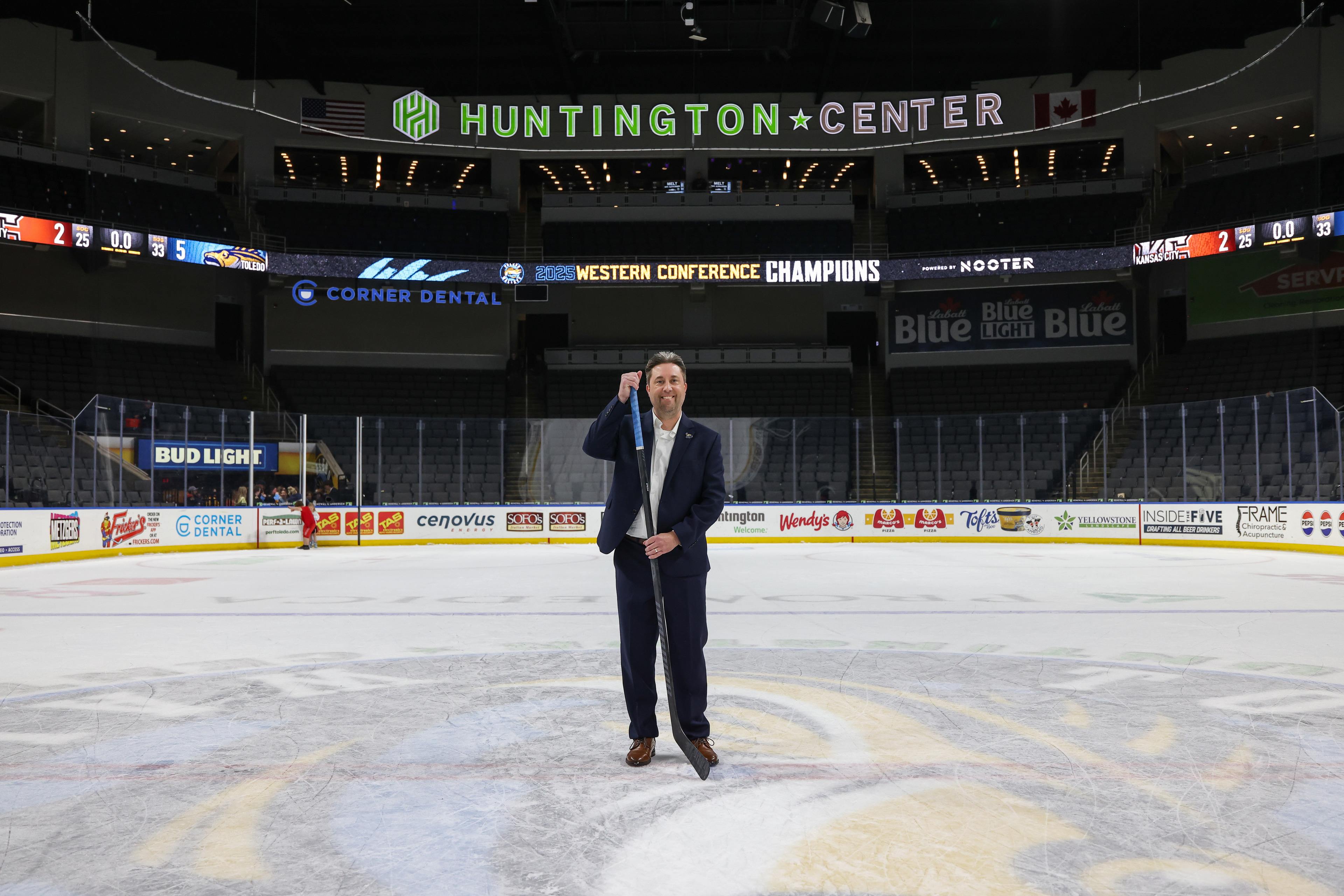 A man stands at center ice of an arena.