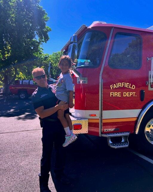 A firefighter holds a child next to a firetruck