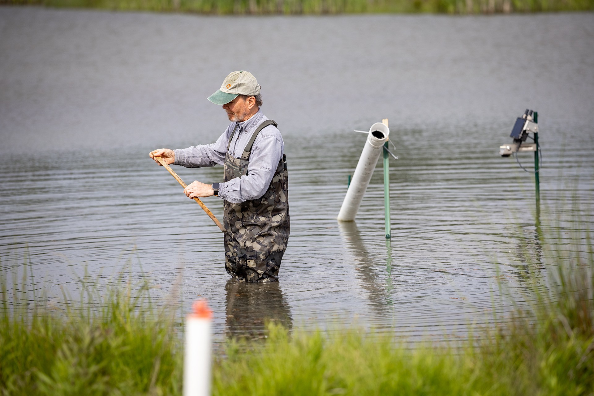 A person stands in knee-deep water taking water samples