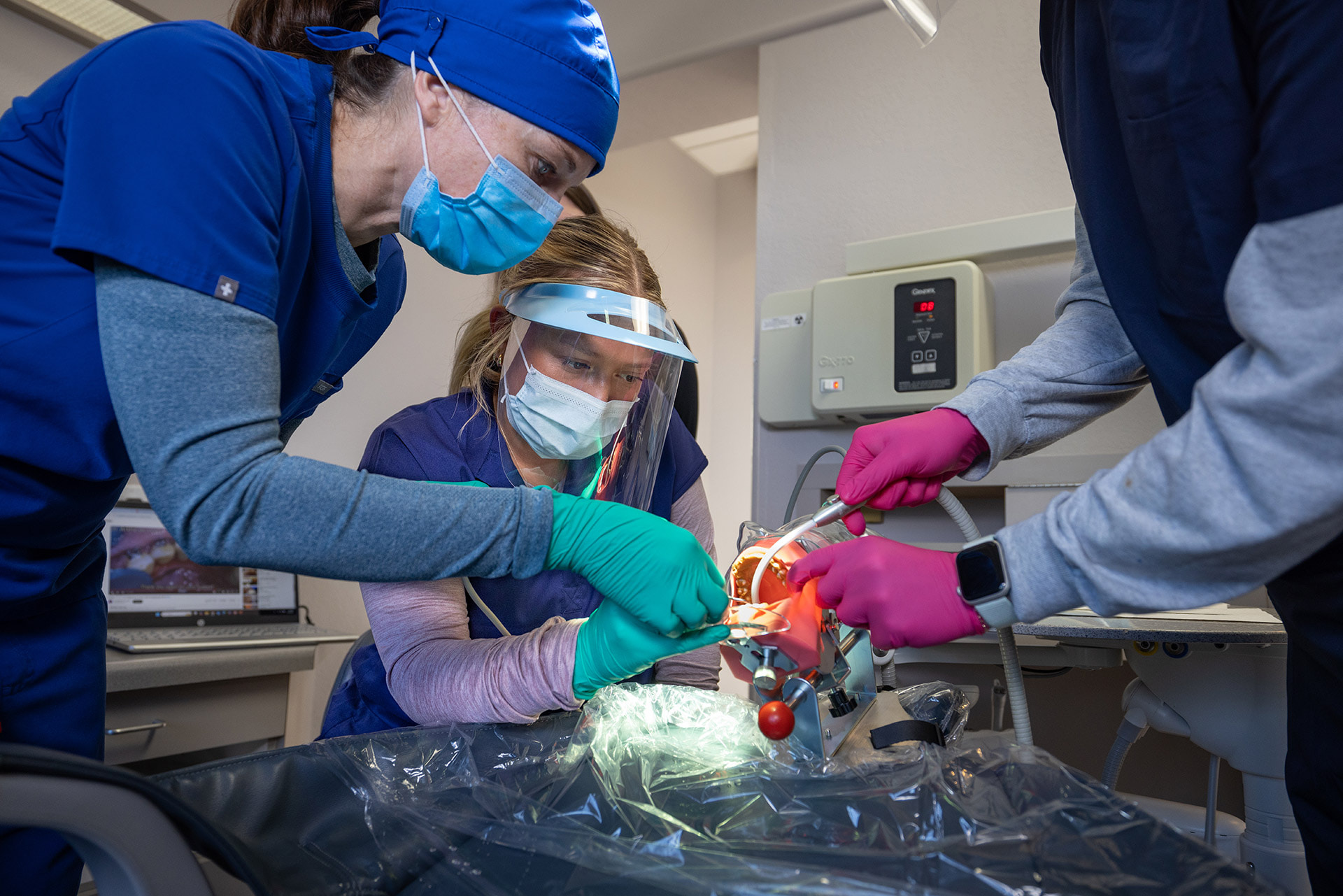 Three people practice cleaning teeth on a dental teeth model.