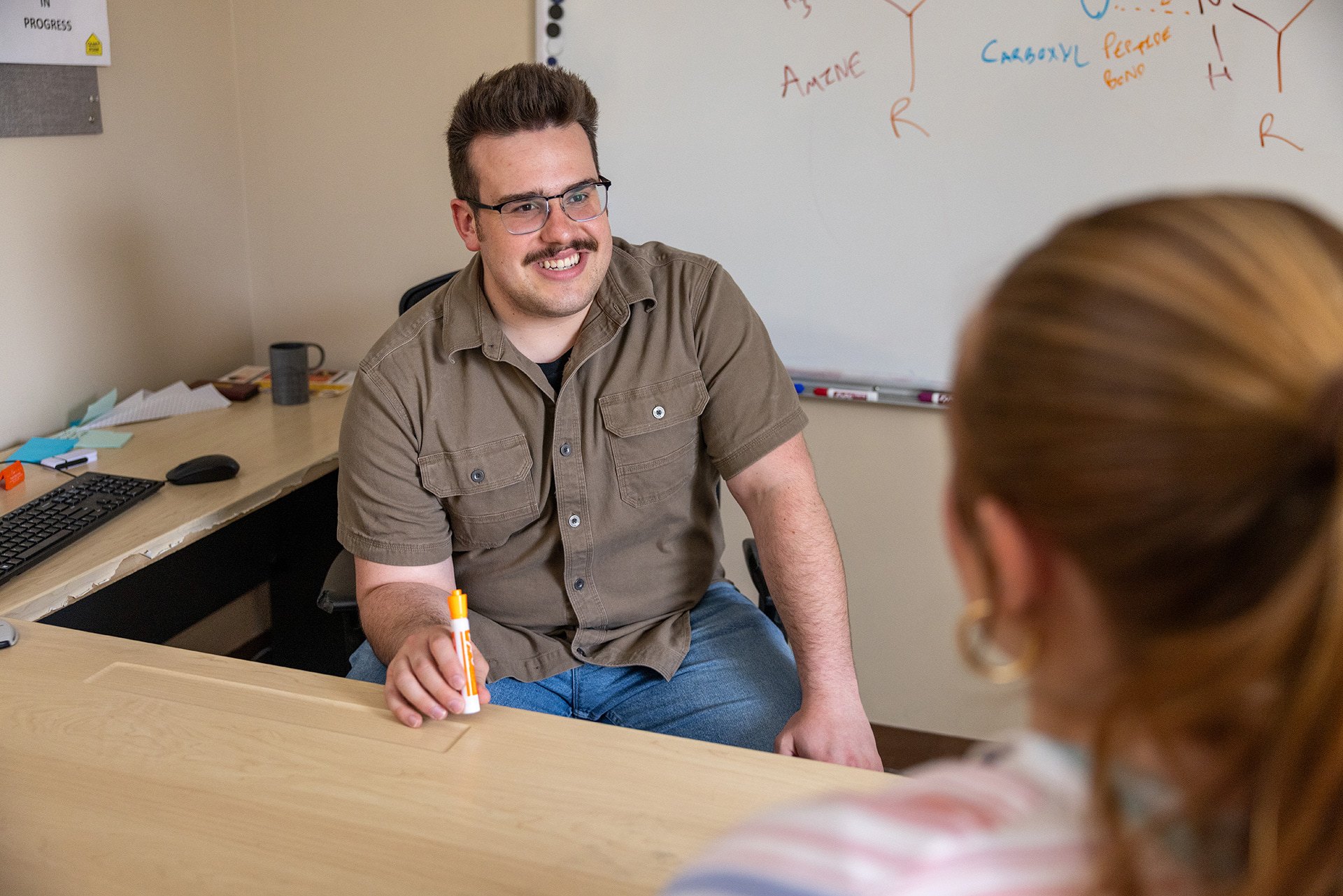 A person sits behind a desk tutoring a student