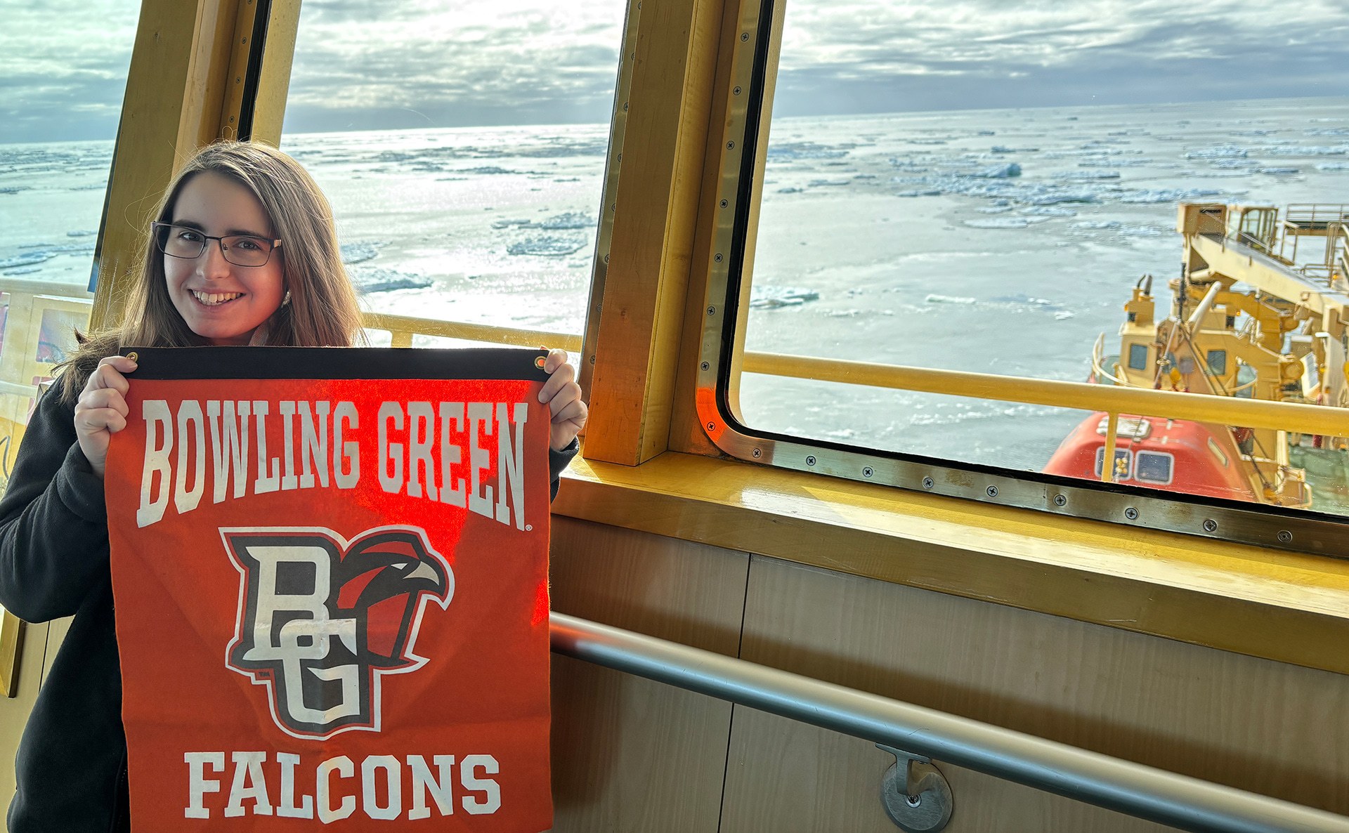 A woman holds an orange flag aboard a ship.