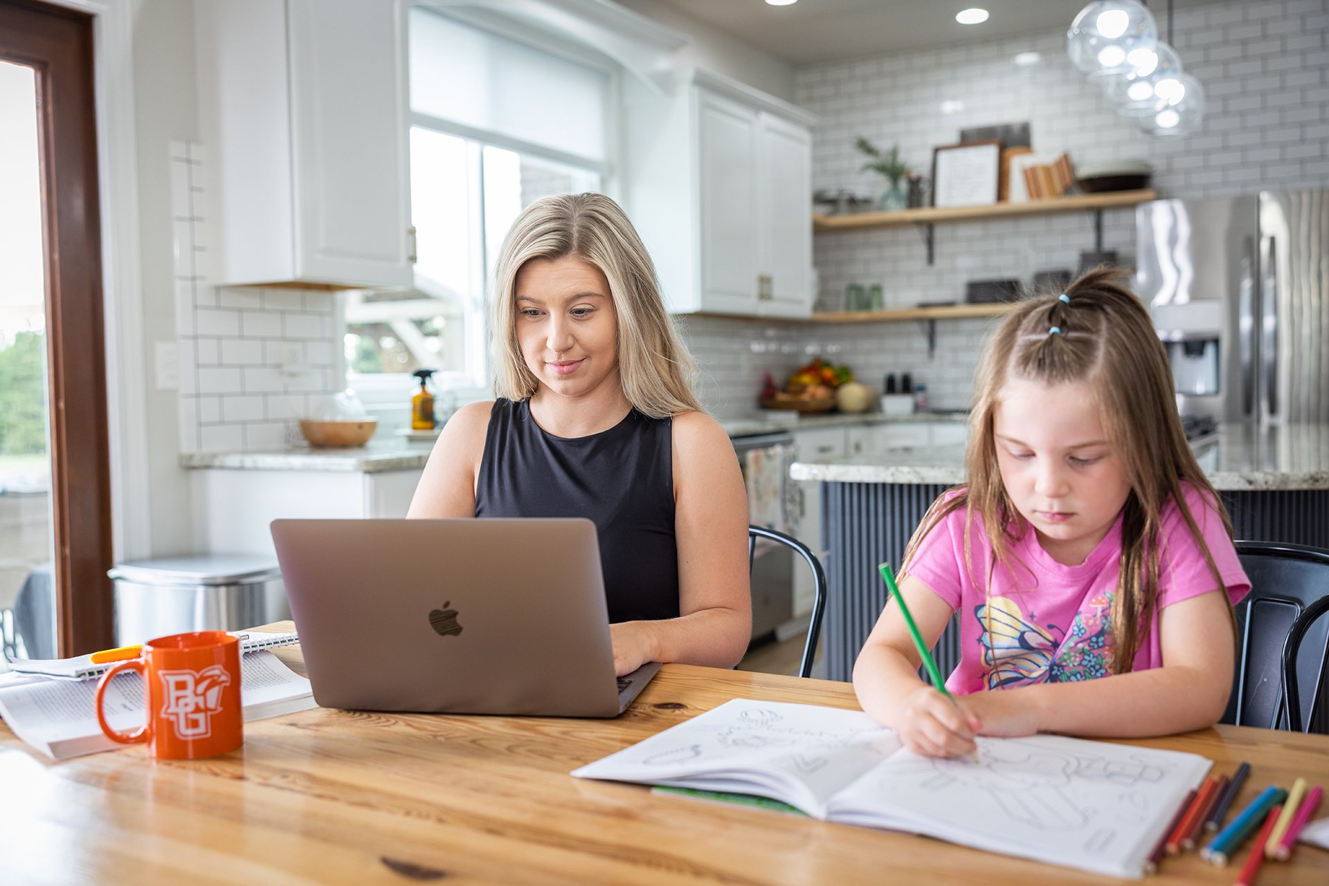 A person works on a laptop while a child colors nearby