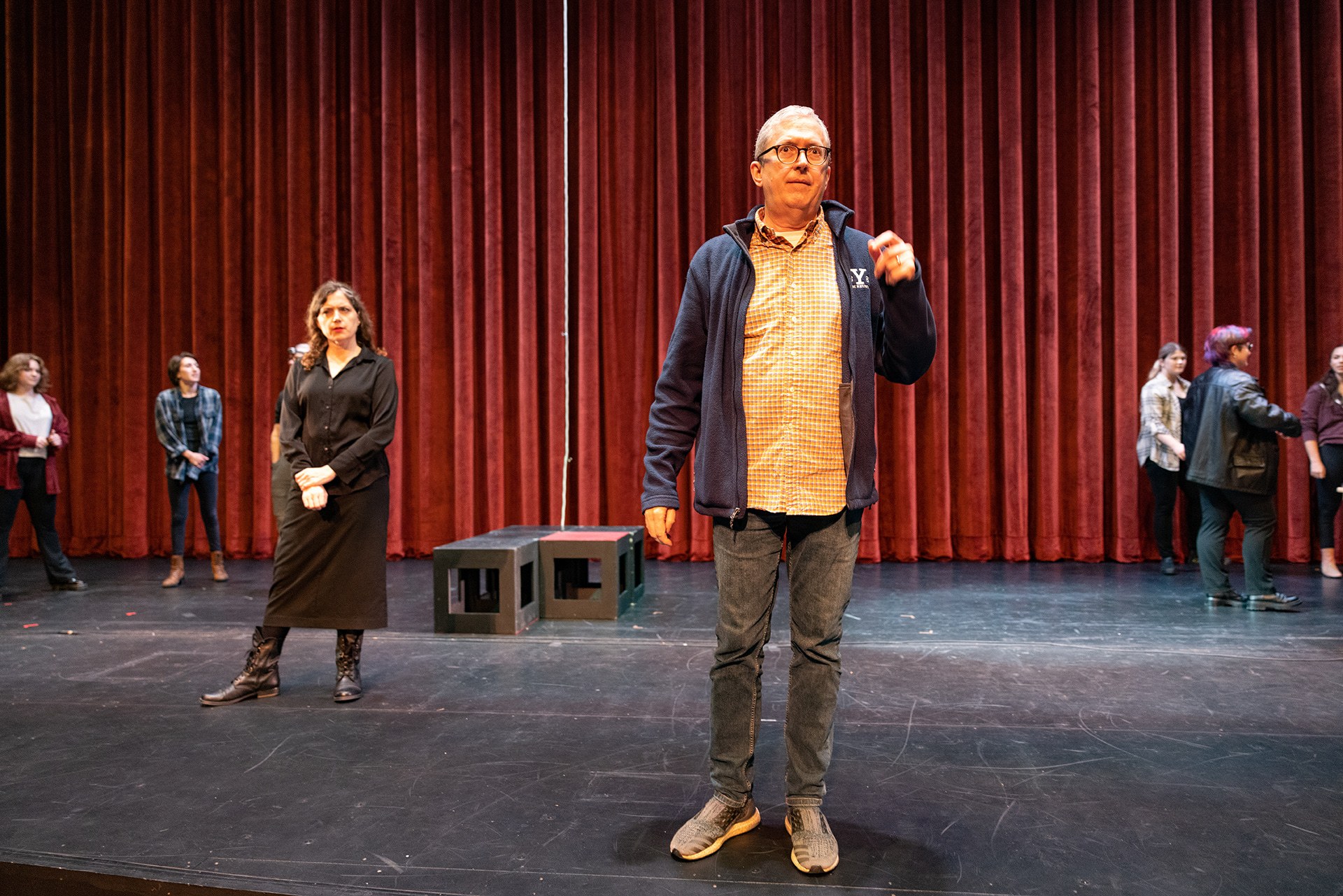 A man addresses a theater ensemble from the stage.