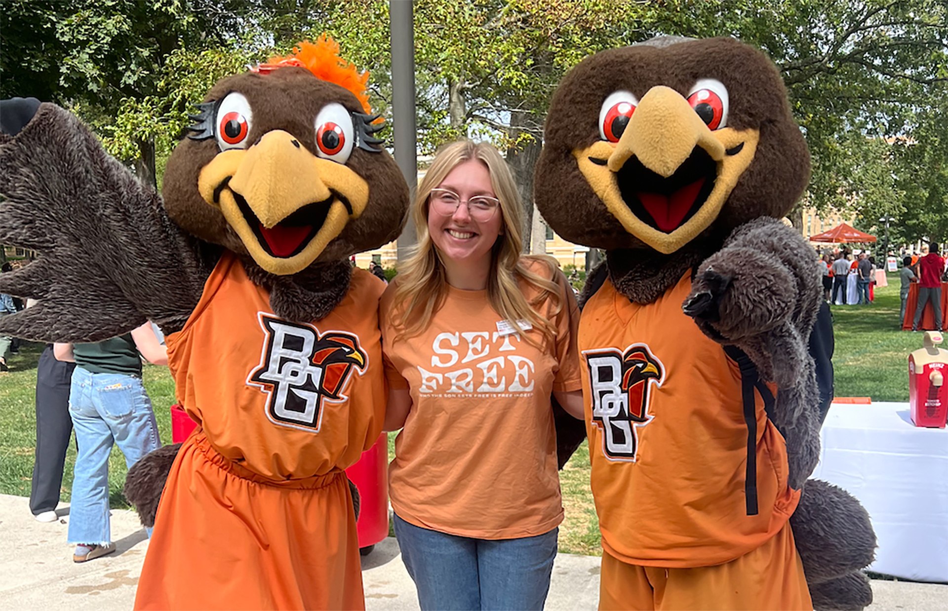 A woman poses for a picture with two falcon mascots