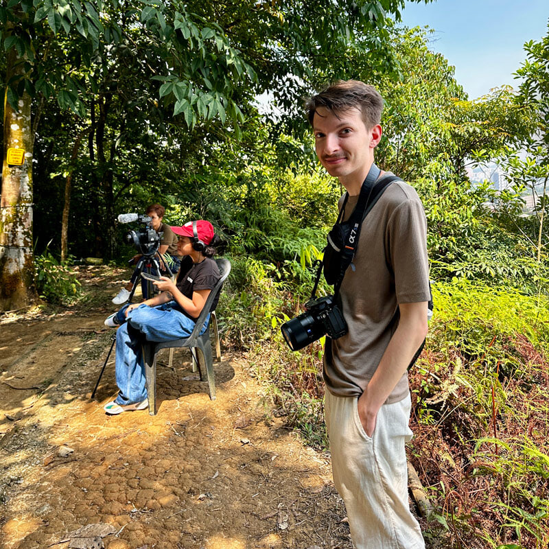 A person stands next to a news crew with a camera around his neck
